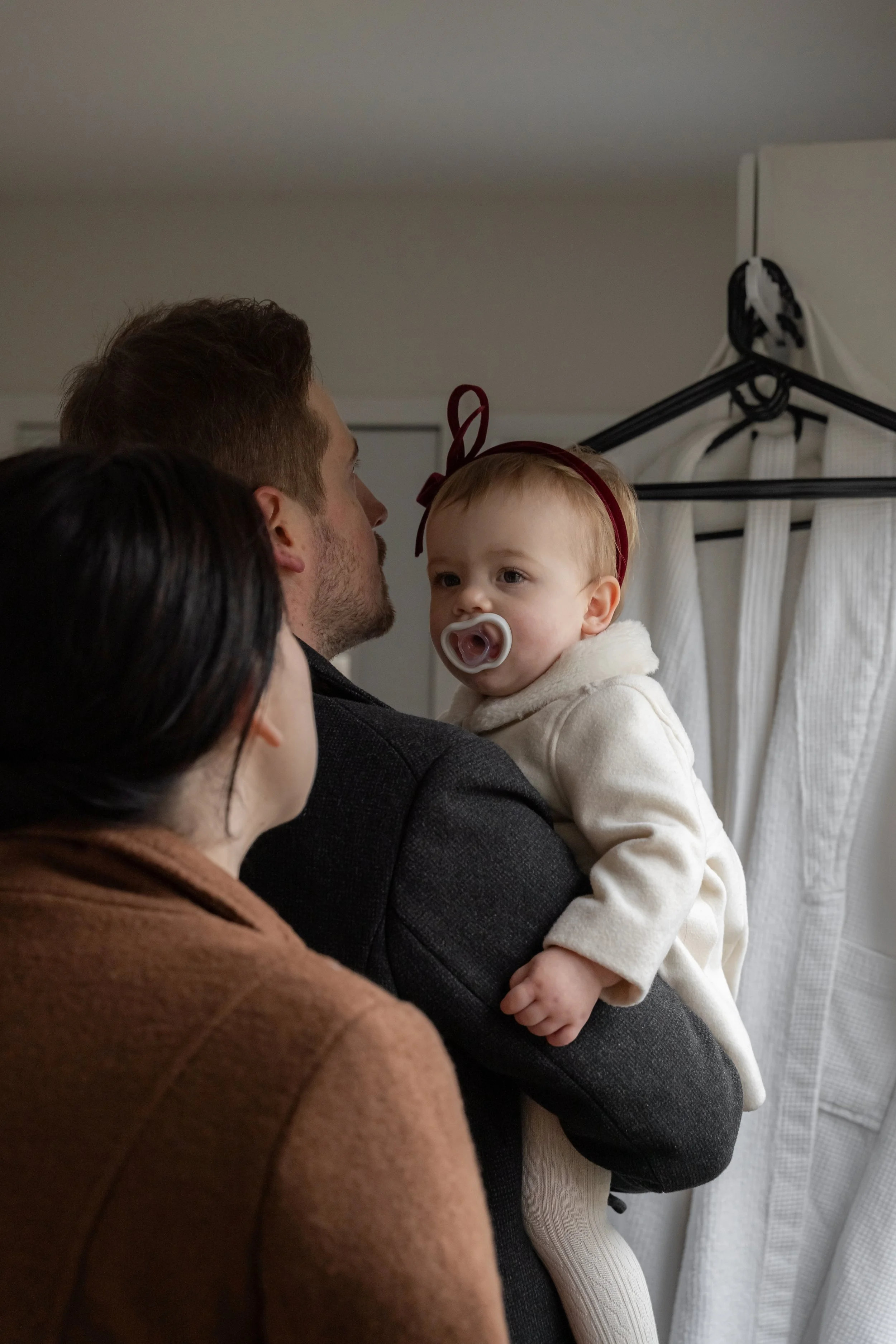 A man holding a young girl with a pacifier, with two women in the foreground and a laundry hanger in the background.