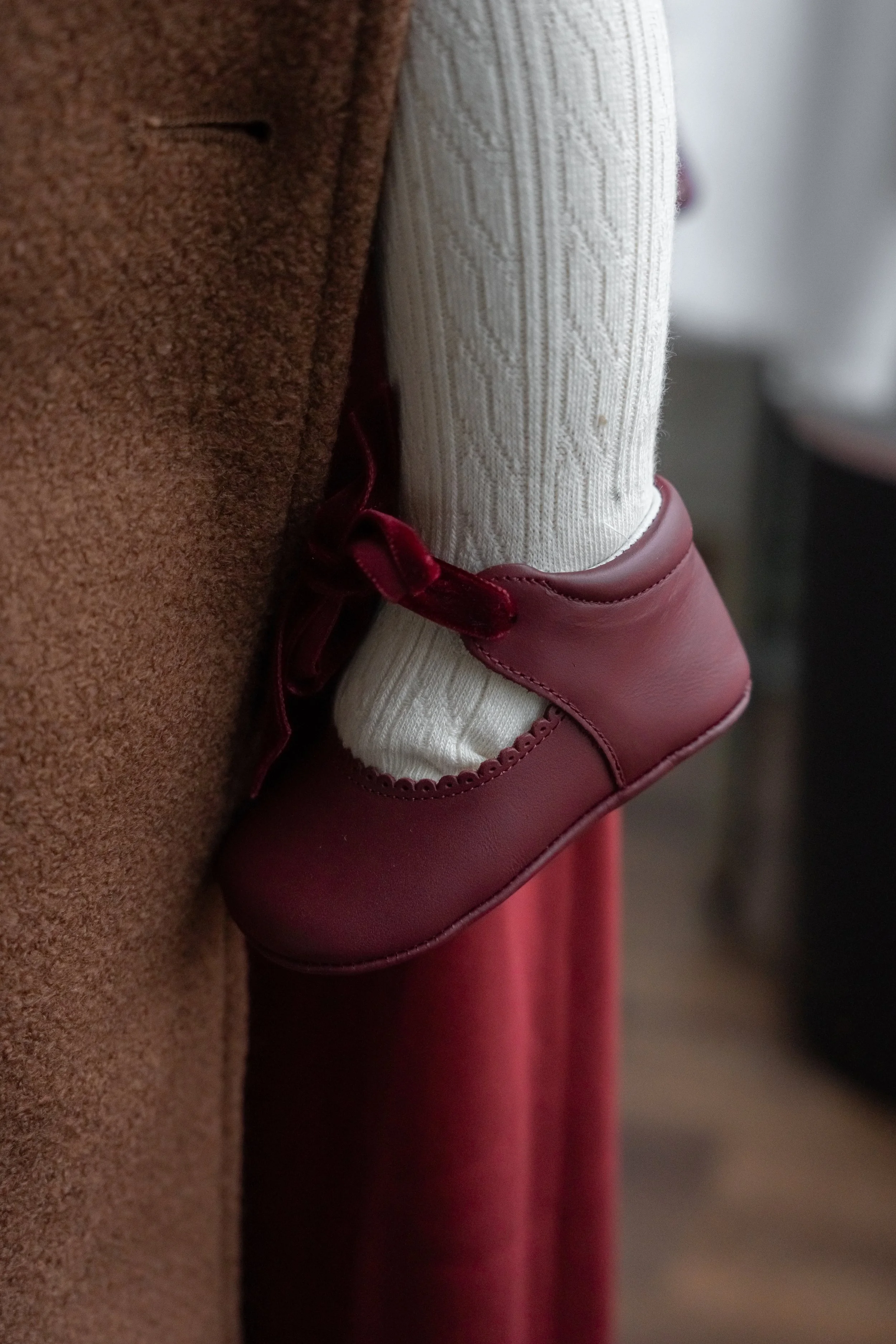 Close-up of a person's foot wearing a burgundy shoe and a white sock with a textured pattern, next to a brown and a red garment.