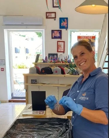 A woman with curly red hair smiles while sitting at a decorated outdoor dining area, holding a lemon wedge.