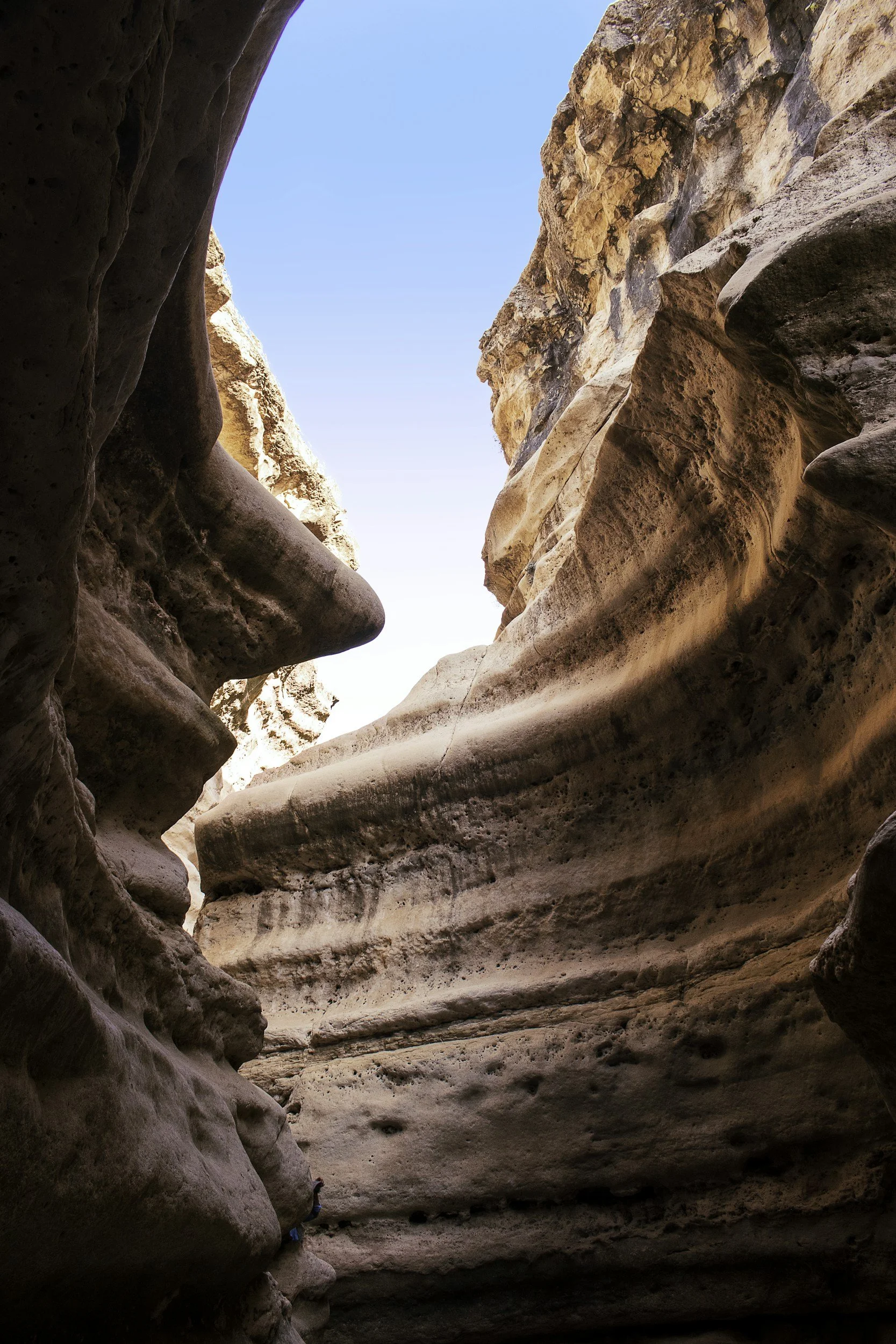 View of side wall of warm earth-tone red and beige canyon looking upwards towards bright blue sky.