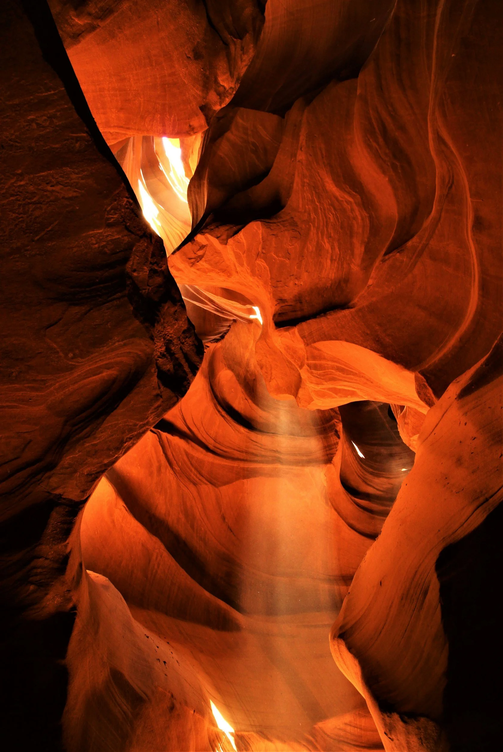 View of warm deep red canyon walls and warm beams of sunlight shining down from caverns above.