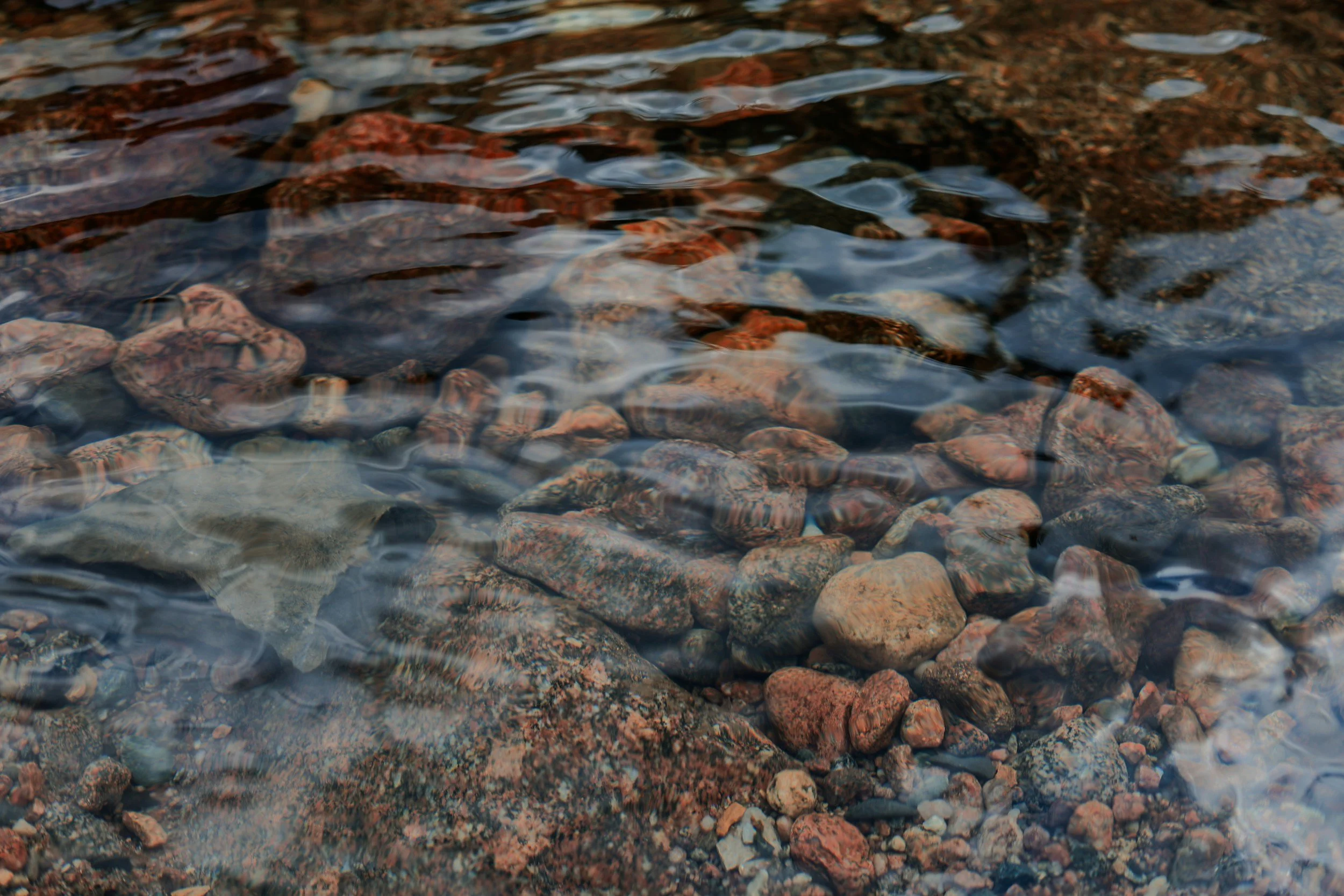 View of river rocks and pebbles through a smooth cool stream with gentle ripples seen in the water.