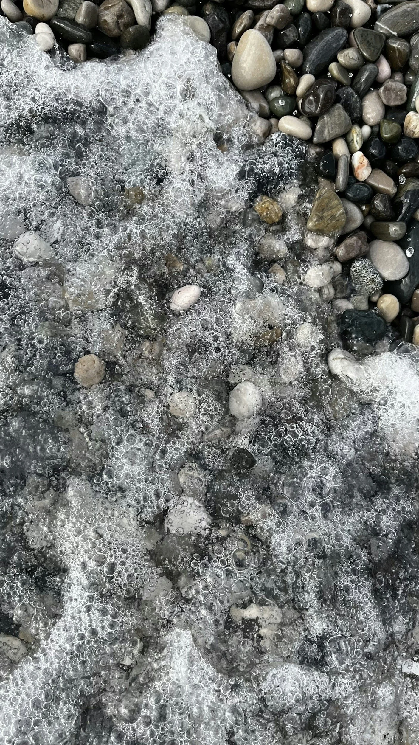 bubbles and waves of water rushing over beach sand and pebbles