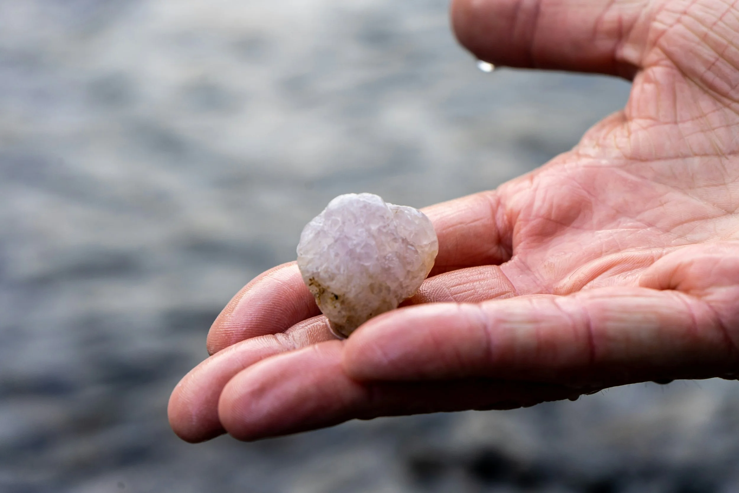 person with wet hand holding quartz stone on beach