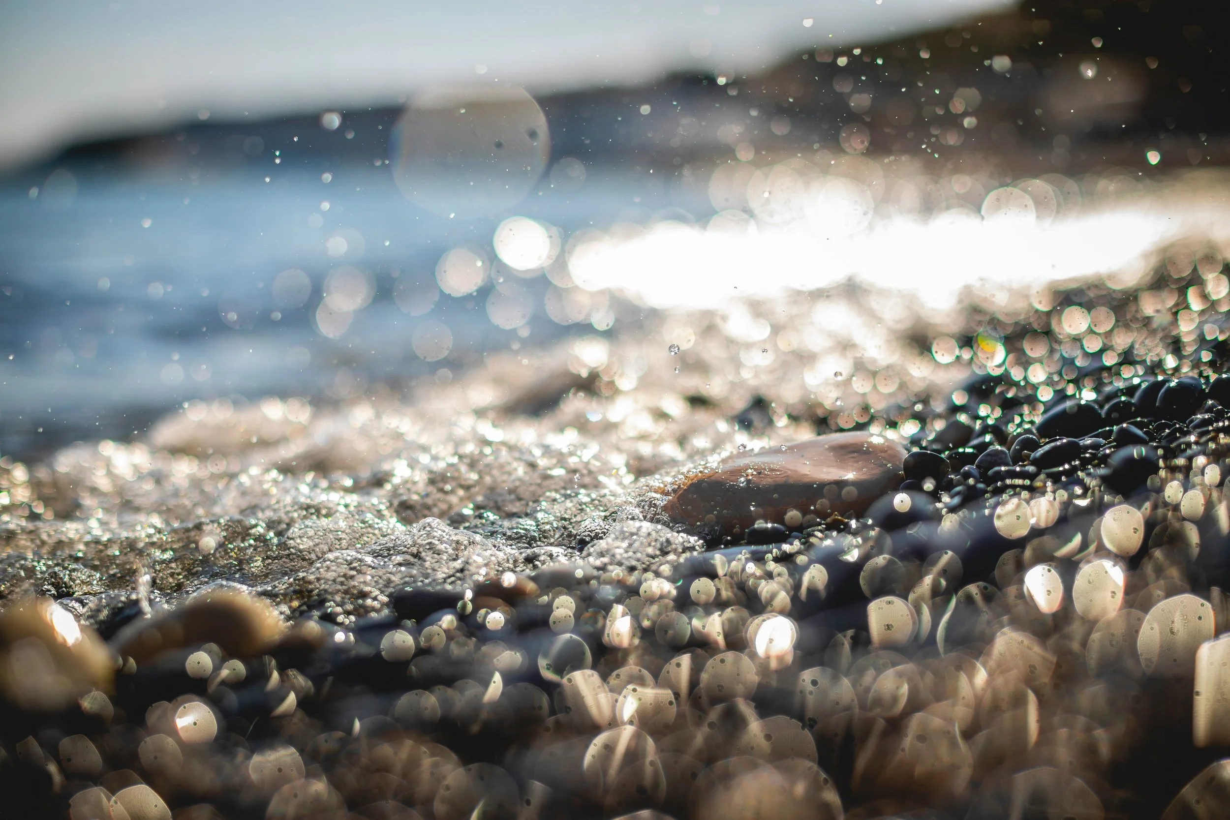 wave spray and bubbles washing over stones and sand in sun on beach