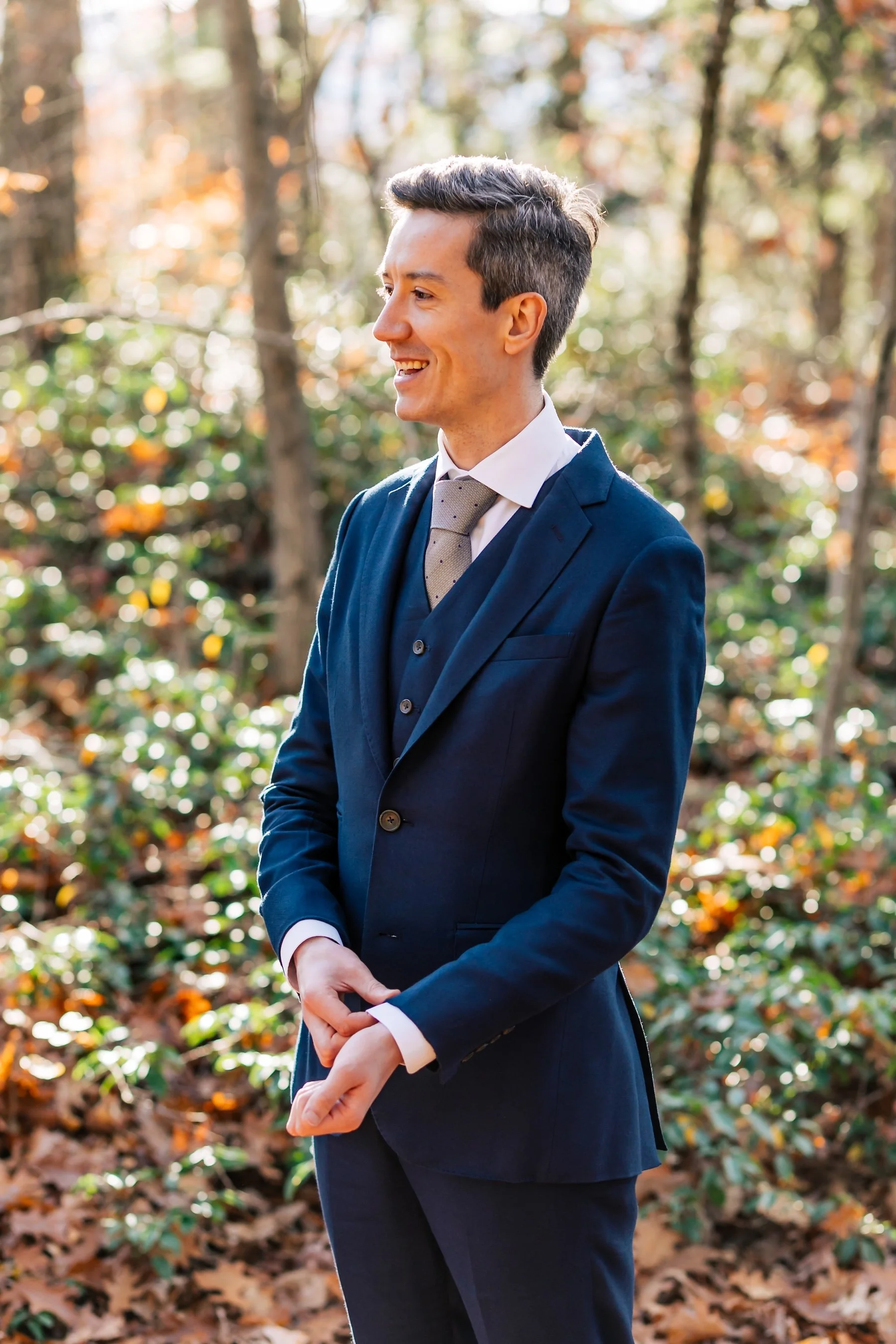Groom in a navy three-piece suit standing among sunlit autumn trees in Western Massachusetts.