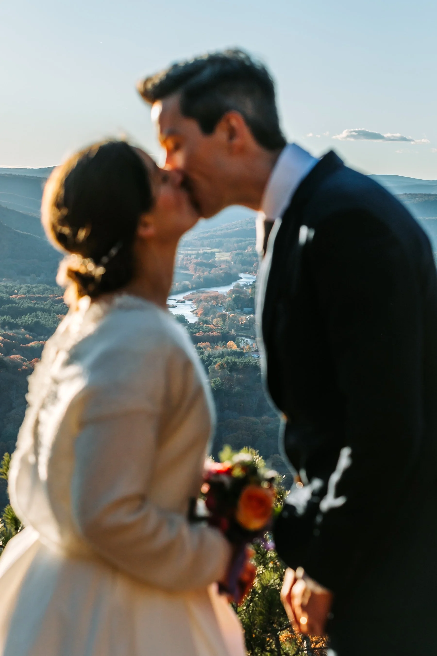 Newlyweds embracing at a scenic High Ledges overlook, surrounded by the colorful fall mountains of New England.