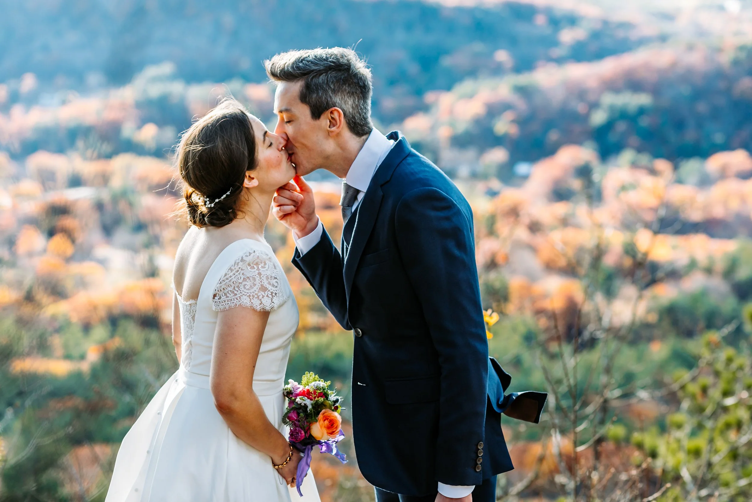 Newlyweds kissing in warm evening light above an autumn-colored valley in Western Massachusetts.