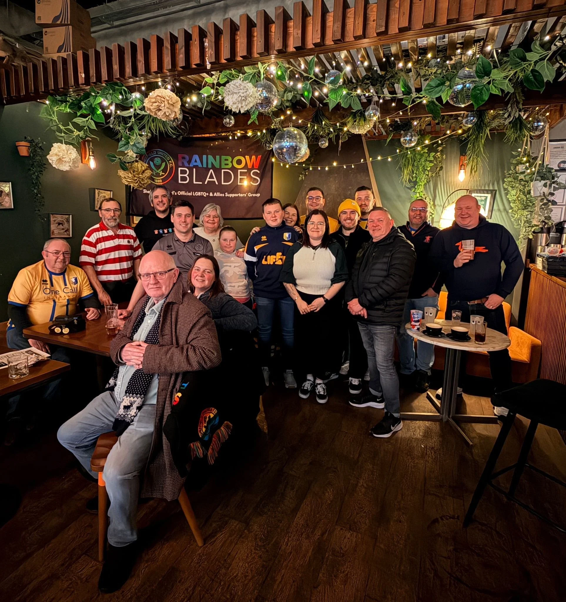 Members of Rainbow Blades and Proud Stags gather for a photo, with the Rainbow Blades flag in the background.