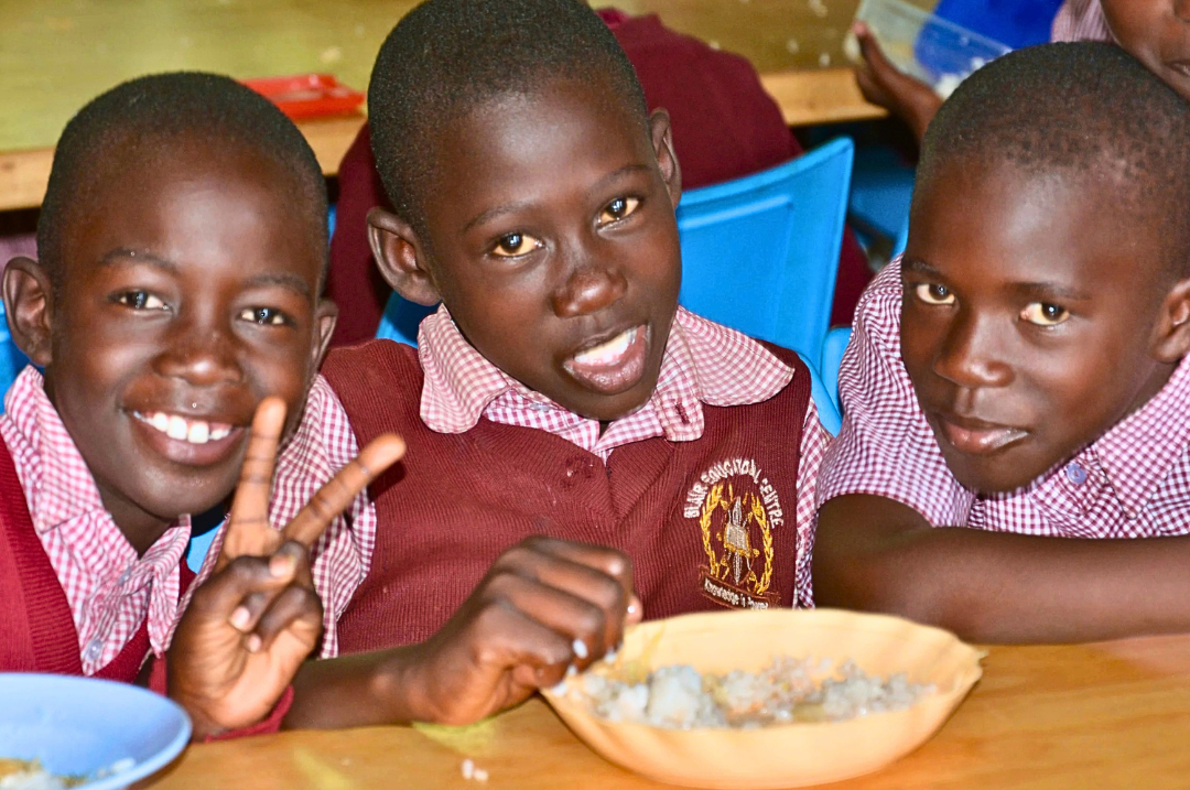 Three boys sitting around a bowl of nutritious food.