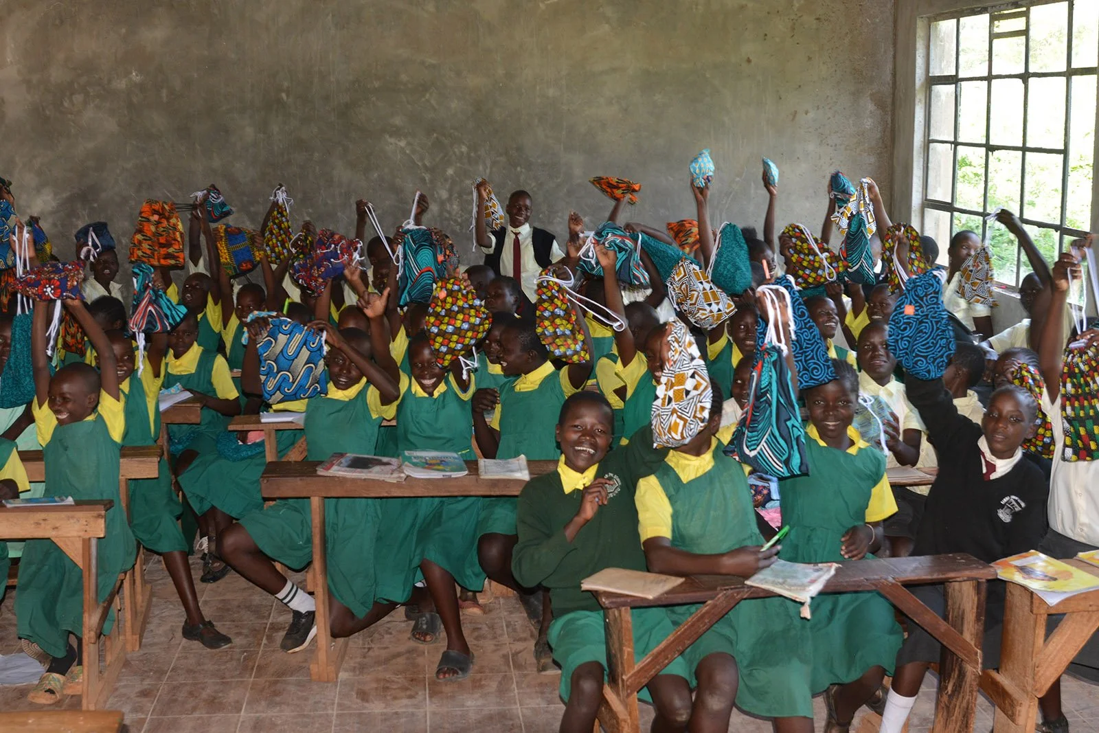 Children in green uniforms hold up their Days for Girls bags