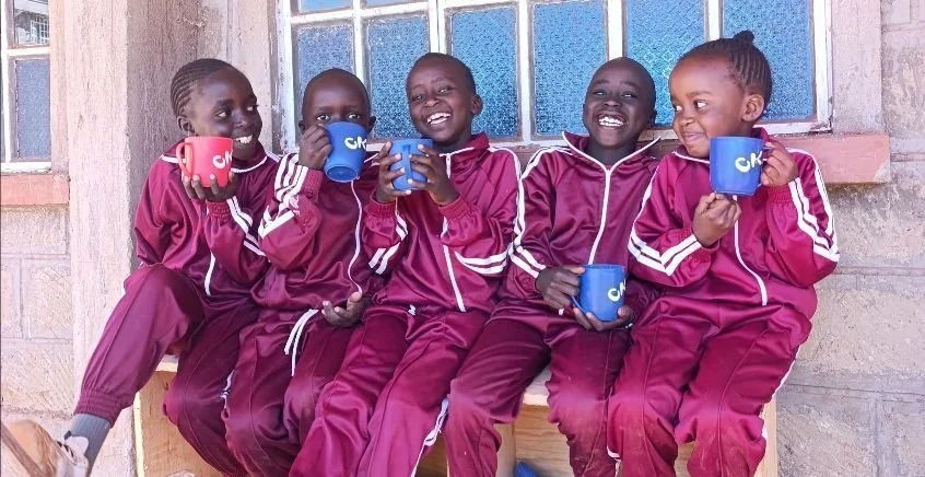 Schoolchildren drinking together from mugs.