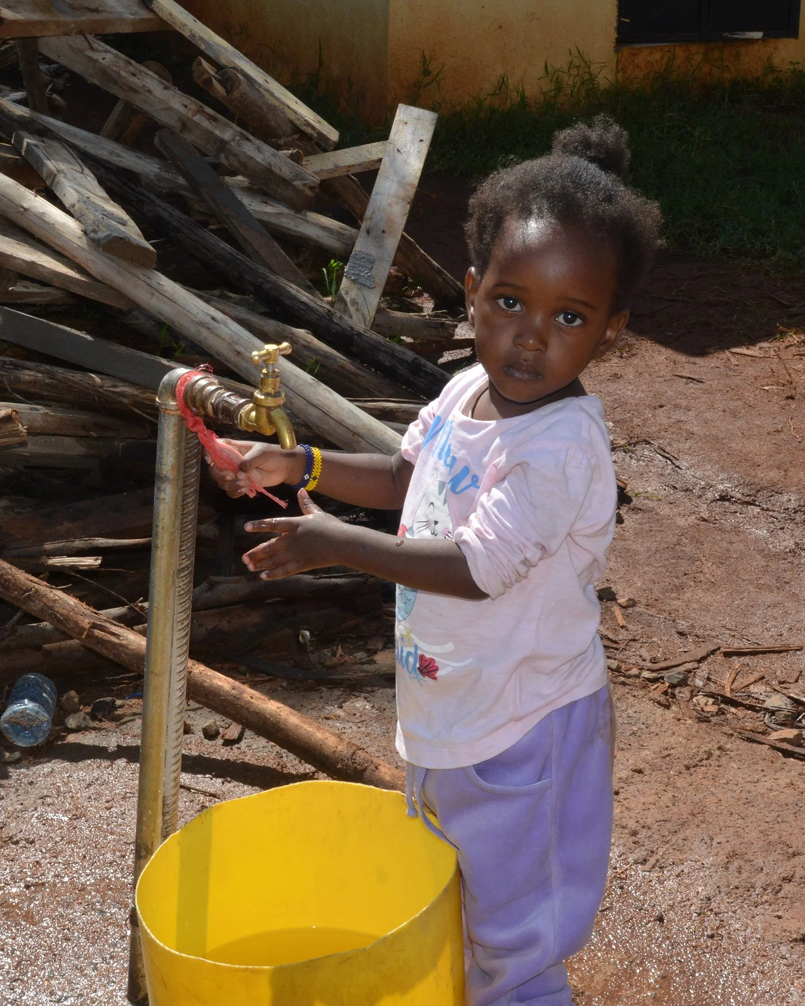 A child washes her hands at an outdoor spigot