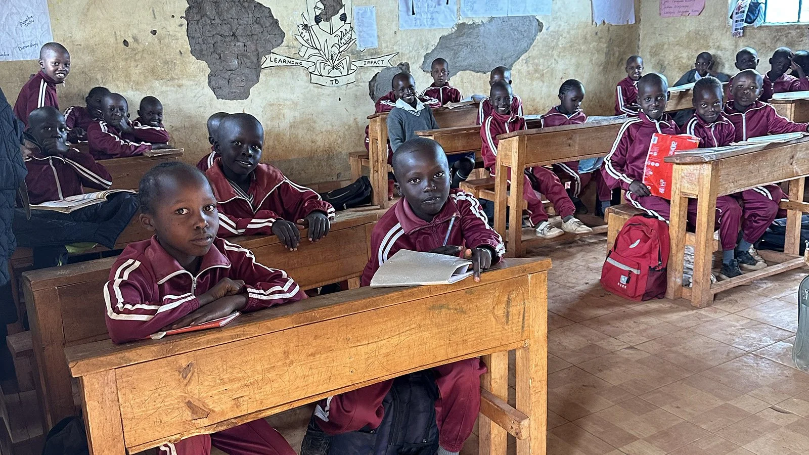 Children in red uniforms sit at school desks