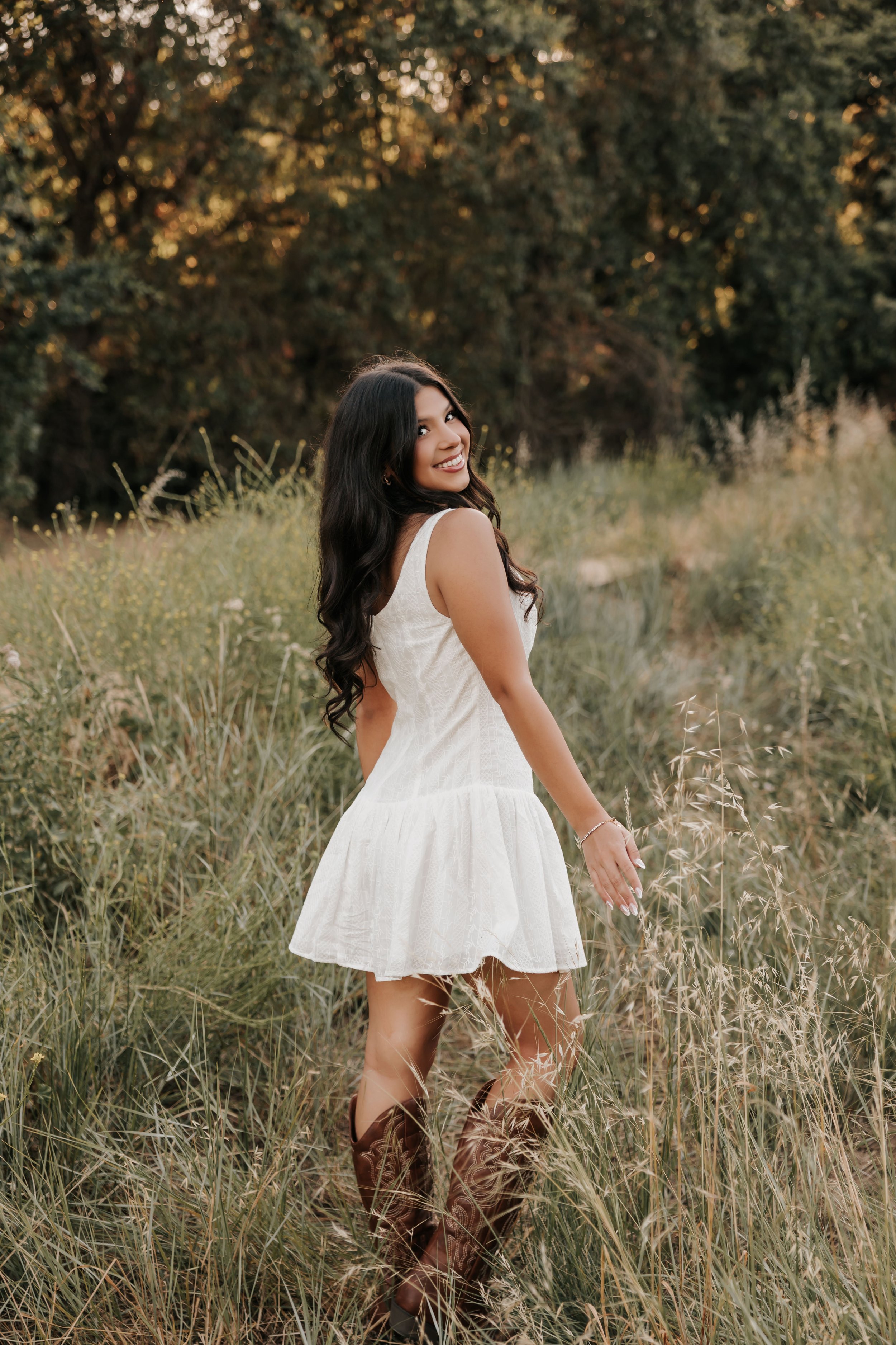 Young woman looking back while walking through tall grass in a white dress.