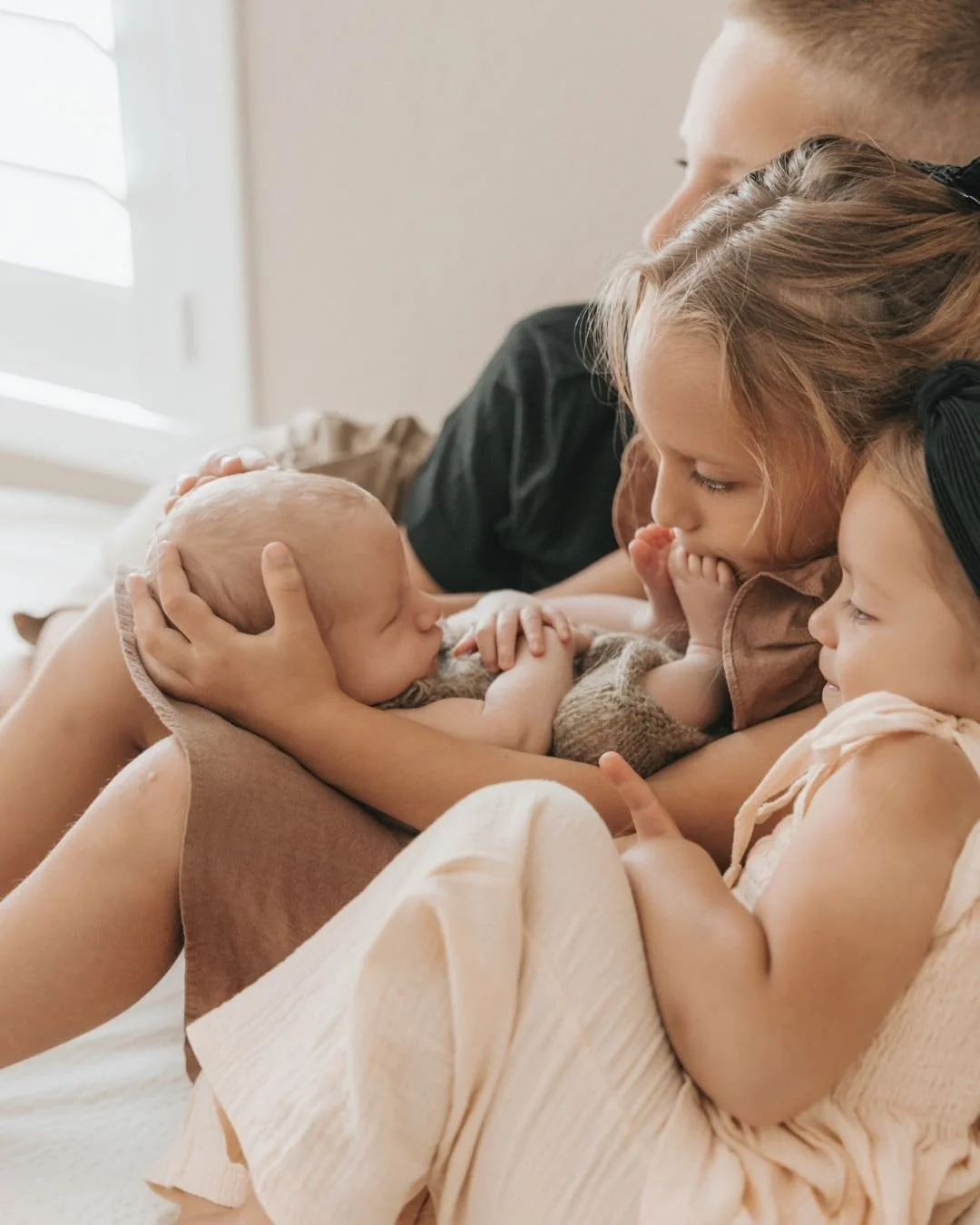 A family of three, including a baby, mother, and two young children, sharing an intimate moment together indoors.