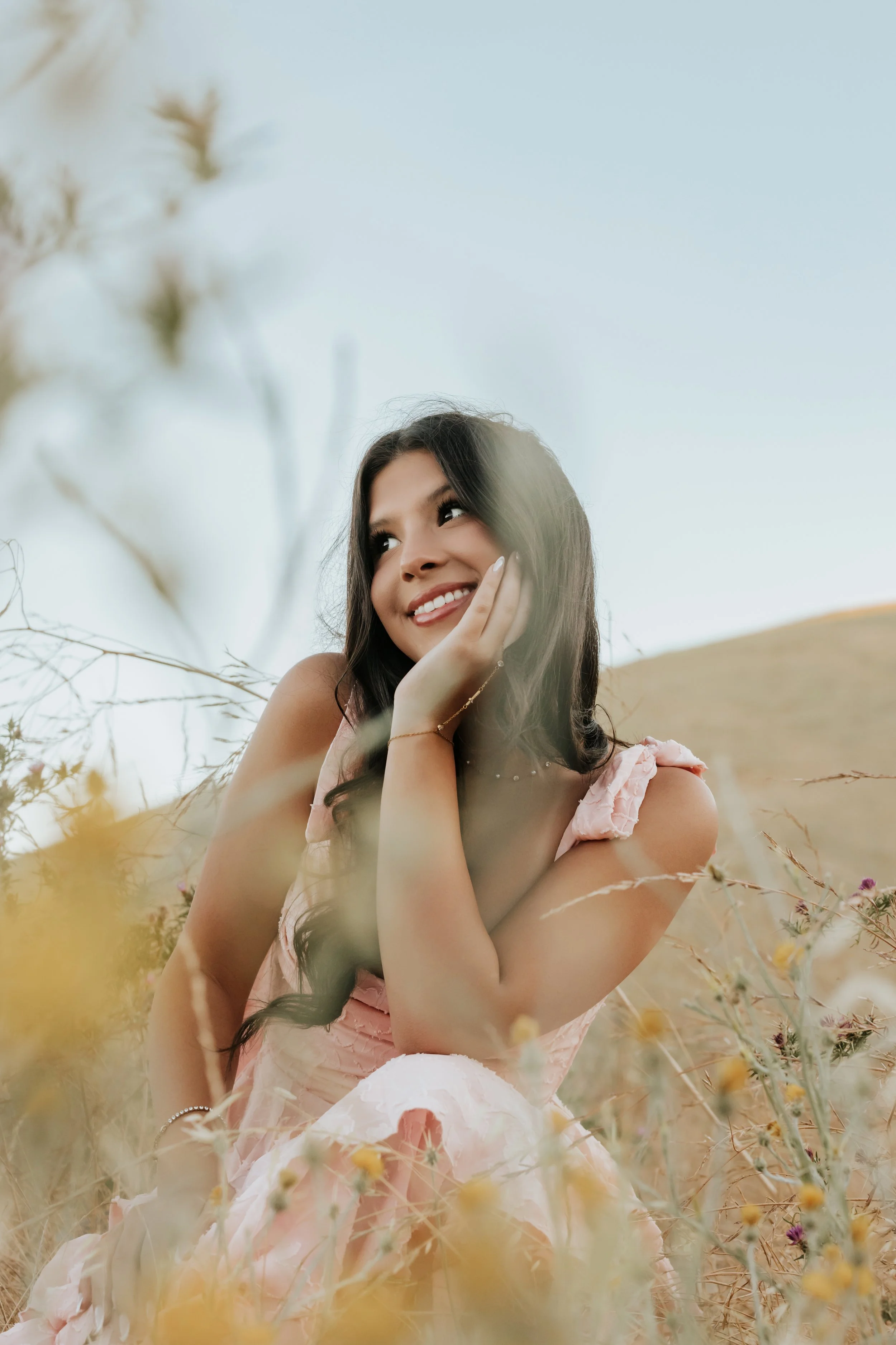 Young woman smiling in a pink dress among golden hills.