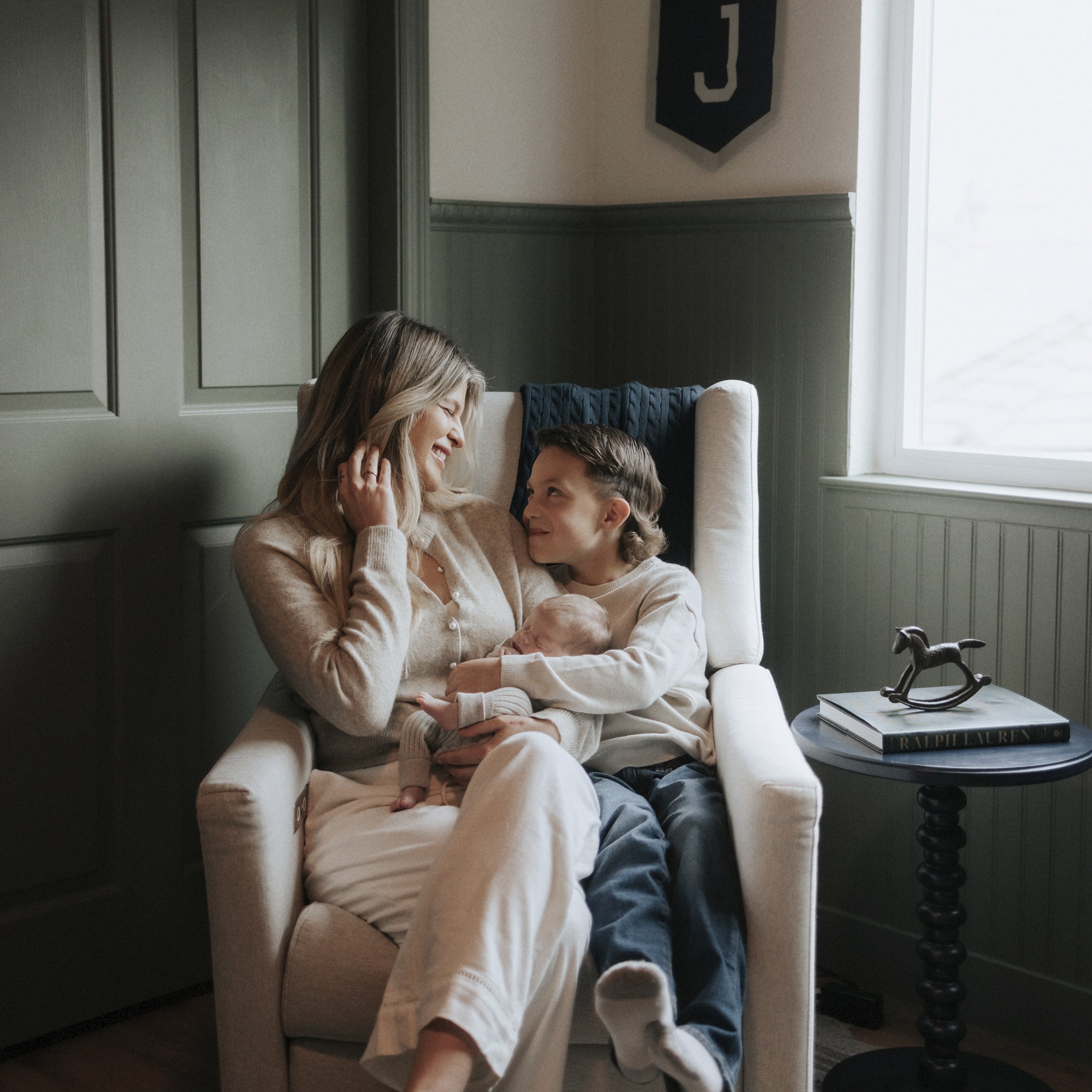 A woman, a young boy, and a newborn baby sitting together in a cozy room, sharing a happy moment.