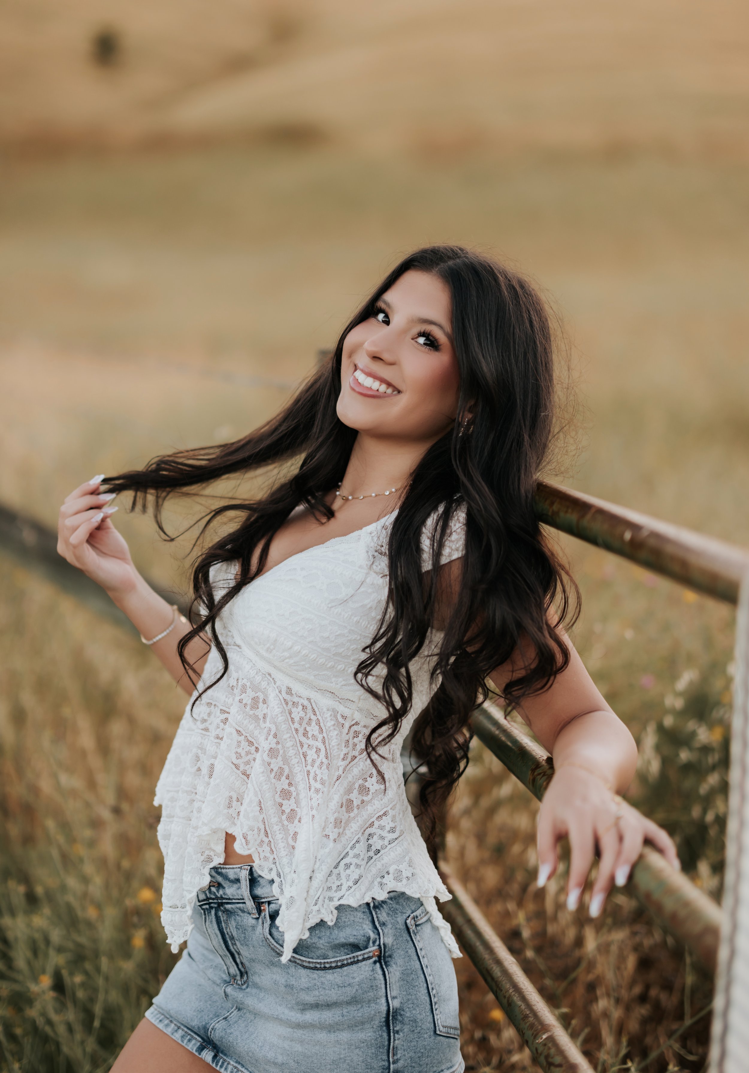 Young woman leaning on a rustic fence in a white top and jeans.