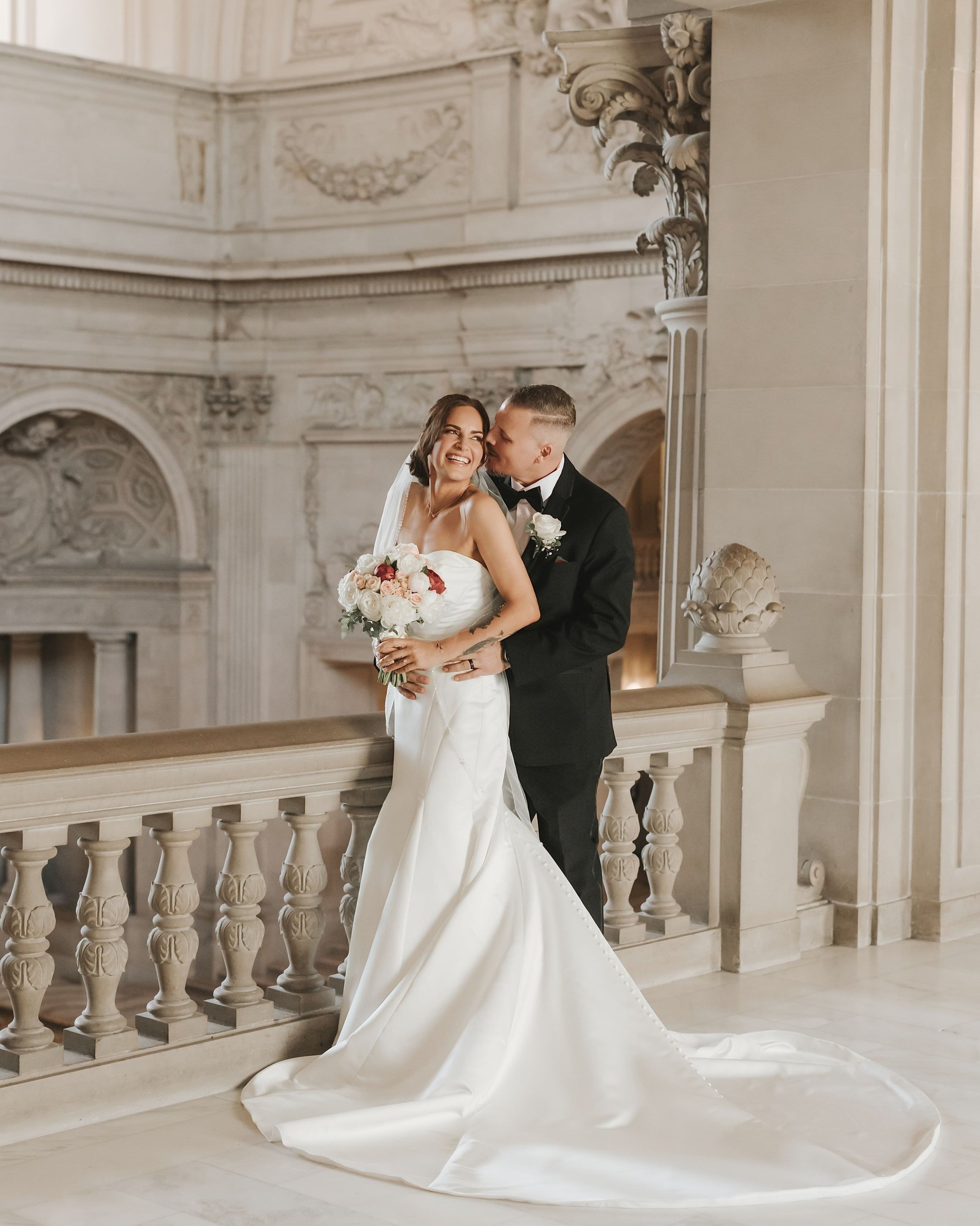 Newlyweds embracing on an ornate City Hall balcony.