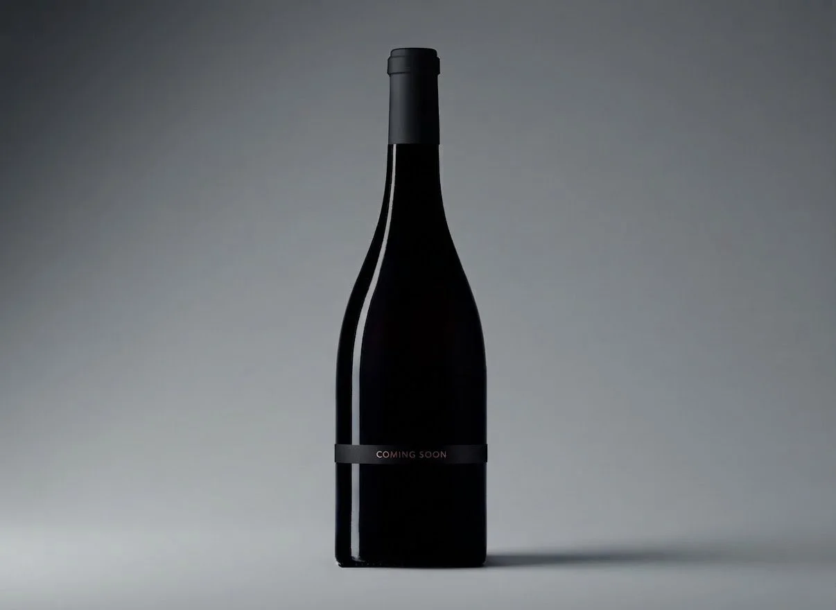 A black wine bottle with a minimalist label that reads 'COMING SOON' on a neutral gray background.