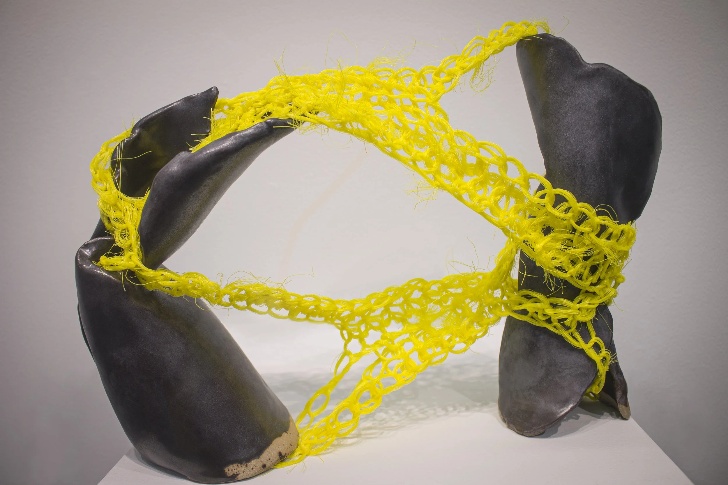 Abrasive Entanglement, 2023, 10in. x 14in. x 6in, Ceramic and unraveled nylon rope.
 
This piece was created by creating opposing movements in two hollow clay forms. The steely finish of the ceramic highlights the creases and indentations. This is co