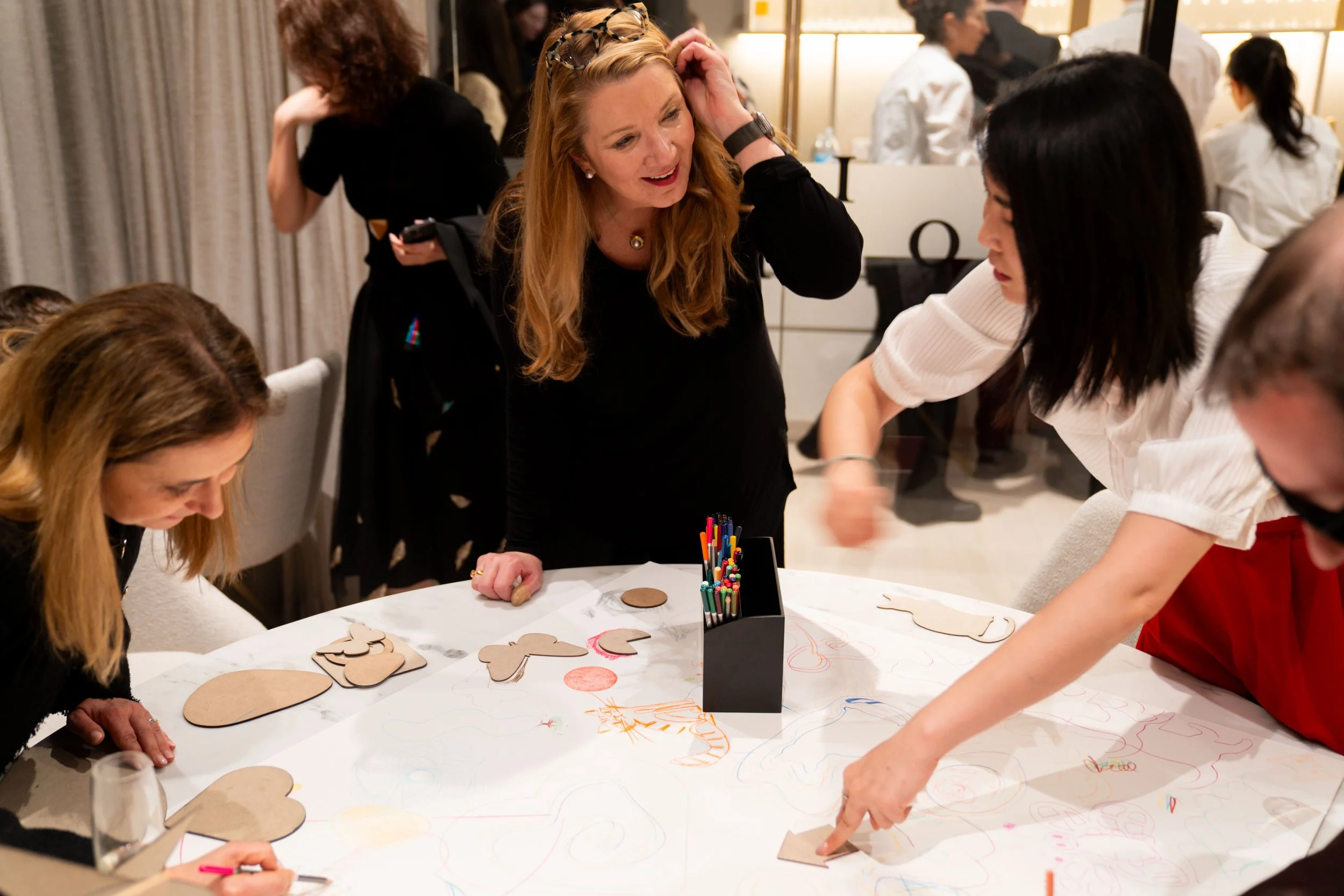 Artist Aly Indermuhle facilitating a participatory art and coloring workshop at a corporate event, with guests engaging in a collaborative creative activity.