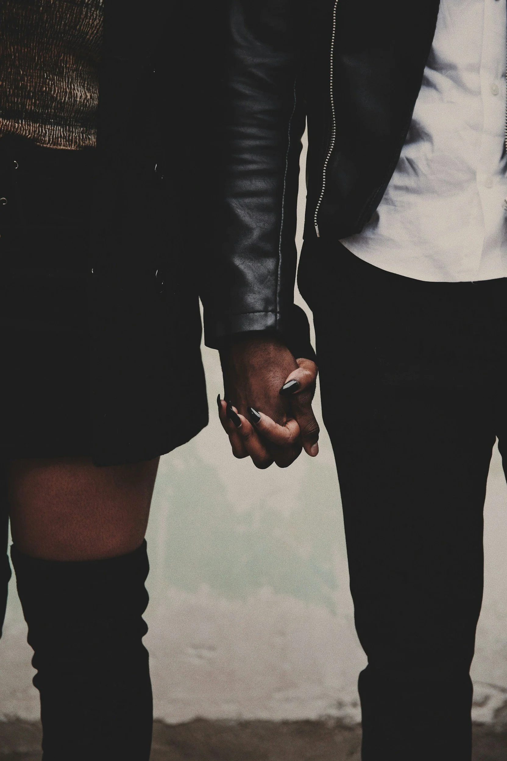 Two people holding hands, dressed in dark clothing, standing close together on a beach.