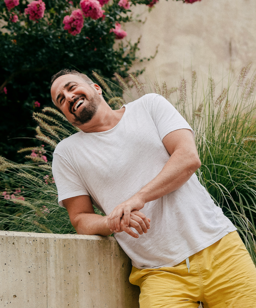Jonas laughing, leaning on a wall in a garden