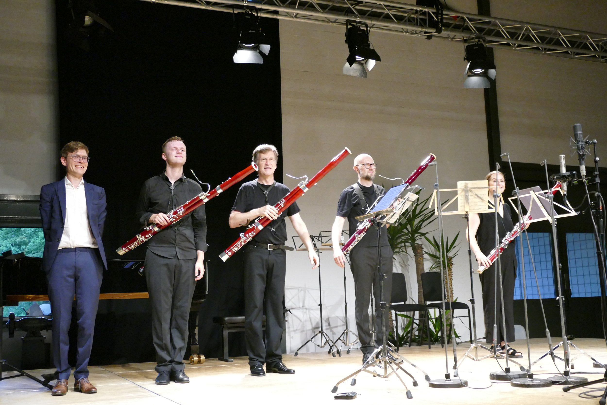 Fünf Musiker auf einer Bühne, einige mit großen Holzblasinstrumenten, bei einem Auftritt in einem Konzertsaal.