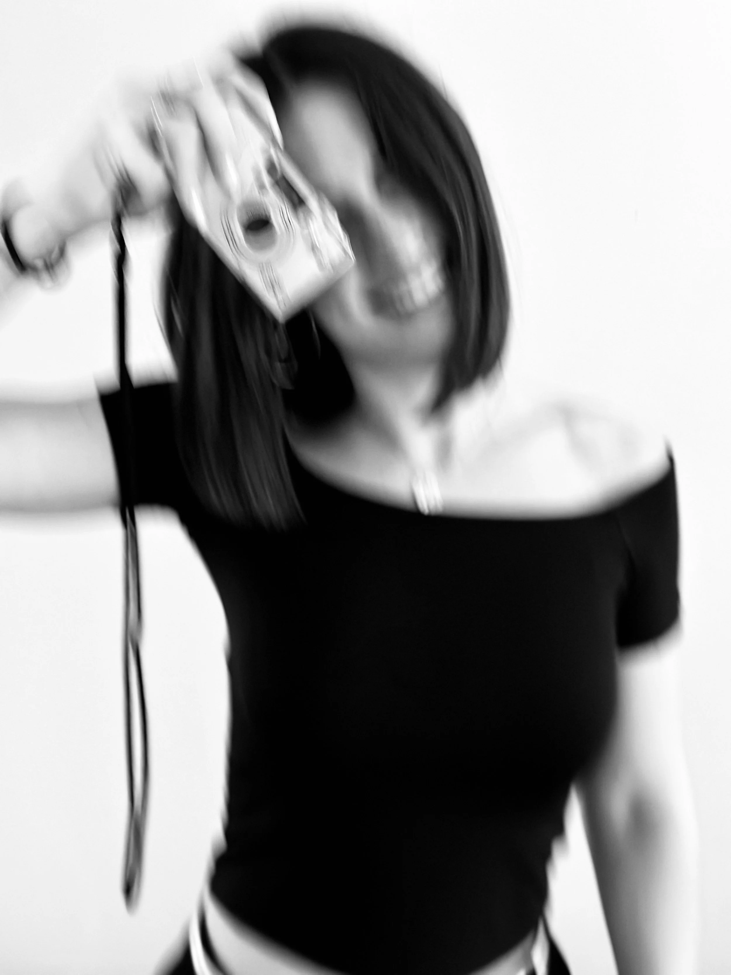 Une personne avec de longs cheveux noirs tient un appareil photo dans sa main gauche, étant floue dans l'image.