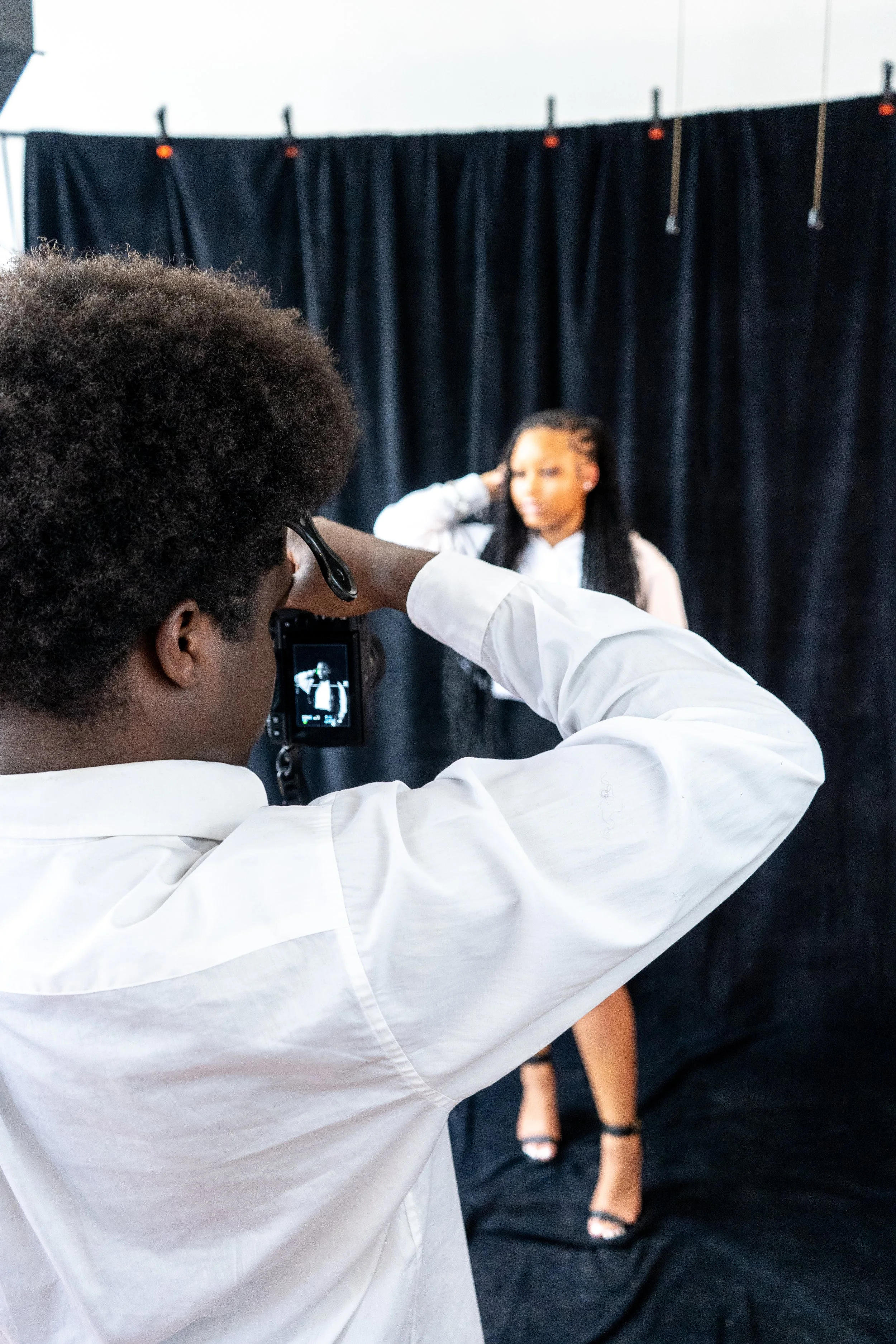A photographer taking a picture of a woman in front of a black curtain backdrop.