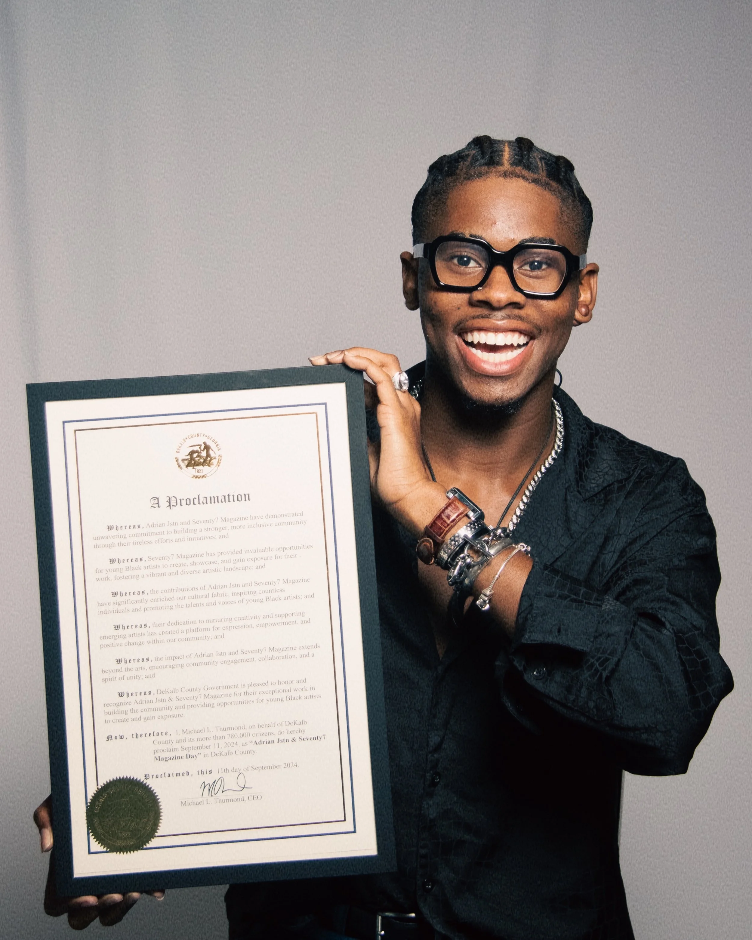 Adrian Jstn young man with glasses, smiling broadly, holding a framed proclamation certificate.