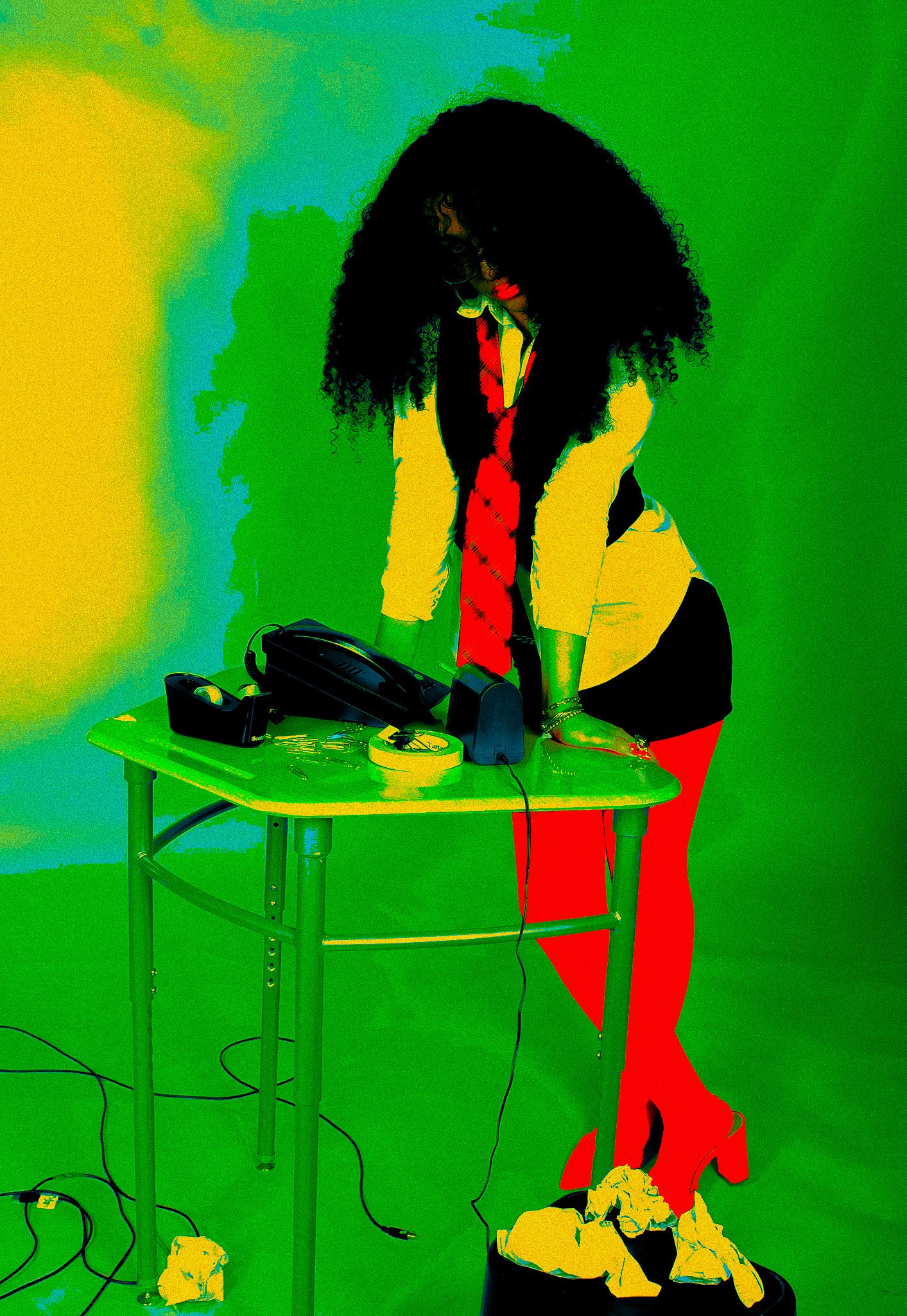 A woman with curly hair and red lipstick leaning over a green table with a telephone, remote, and keys, in front of a vibrant, colorful background.