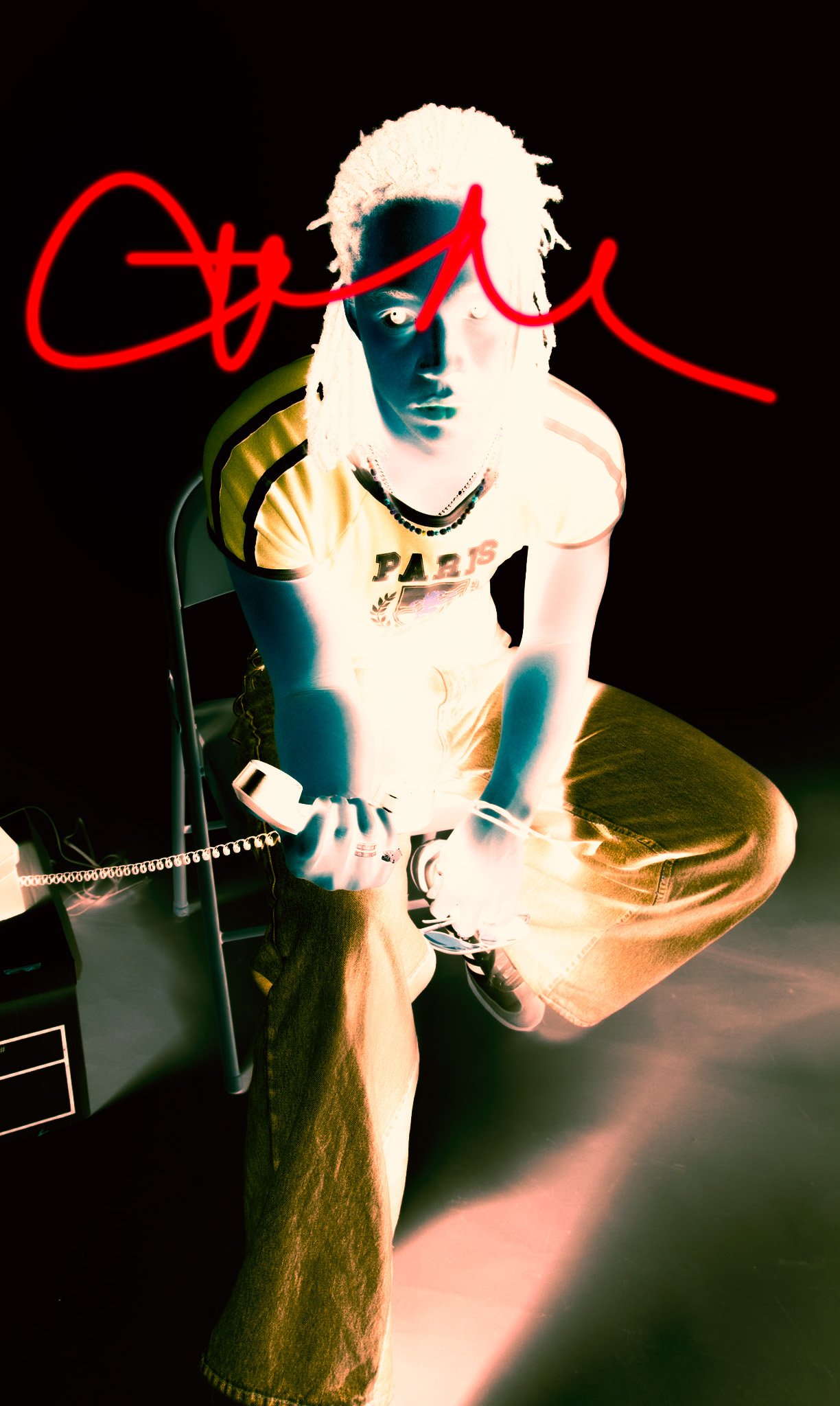 A person with light-colored dreadlocks wearing a yellow Paris-themed T-shirt and jeans, sitting on a chair holding a corded telephone, with a black background and red neon cursive text overlay.