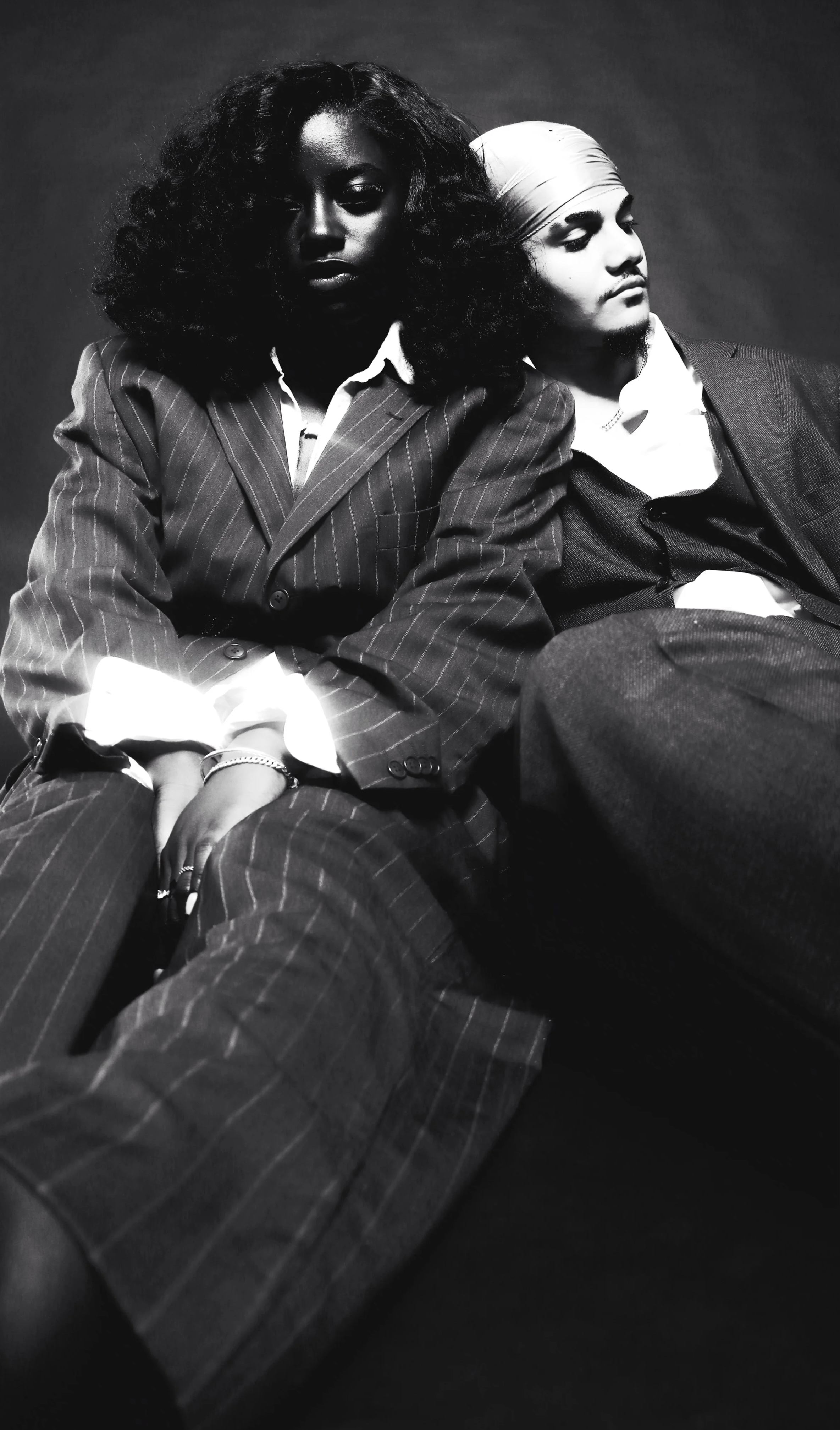 Black and white photo of a woman and a man sitting close, wearing business suits, with serious expressions.