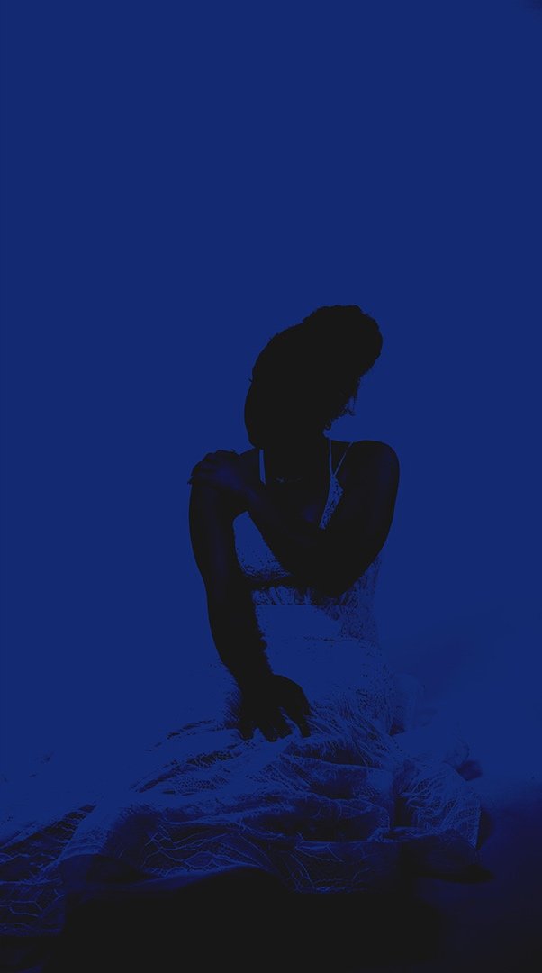 Silhouette of a woman sitting on the floor in a dress against a dark blue background.