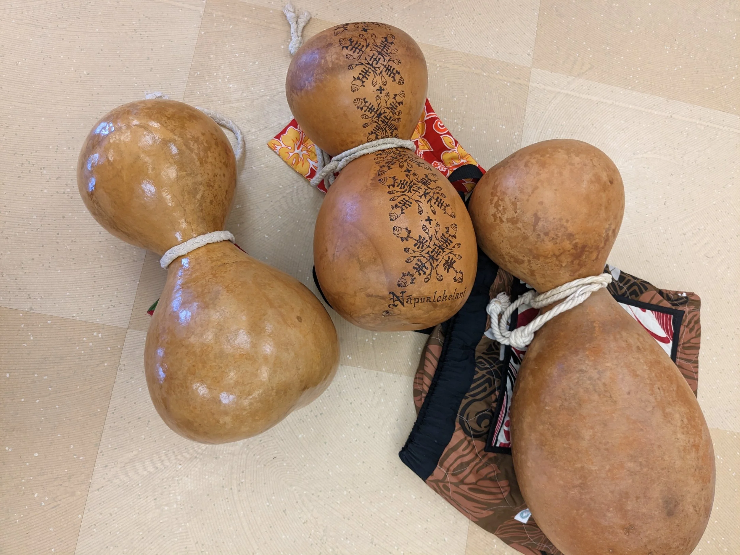 Four traditional musical gourds with carved patterns and signatures, resting on cloths on a tiled floor.