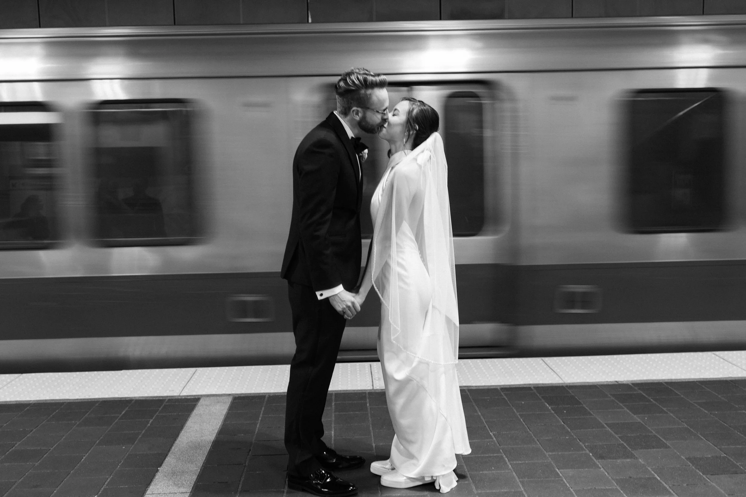 A woman wearing a colorful floral dress is lifted above a crowd at a celebration, smiling and waving a white cloth in an indoor event with many onlookers.
