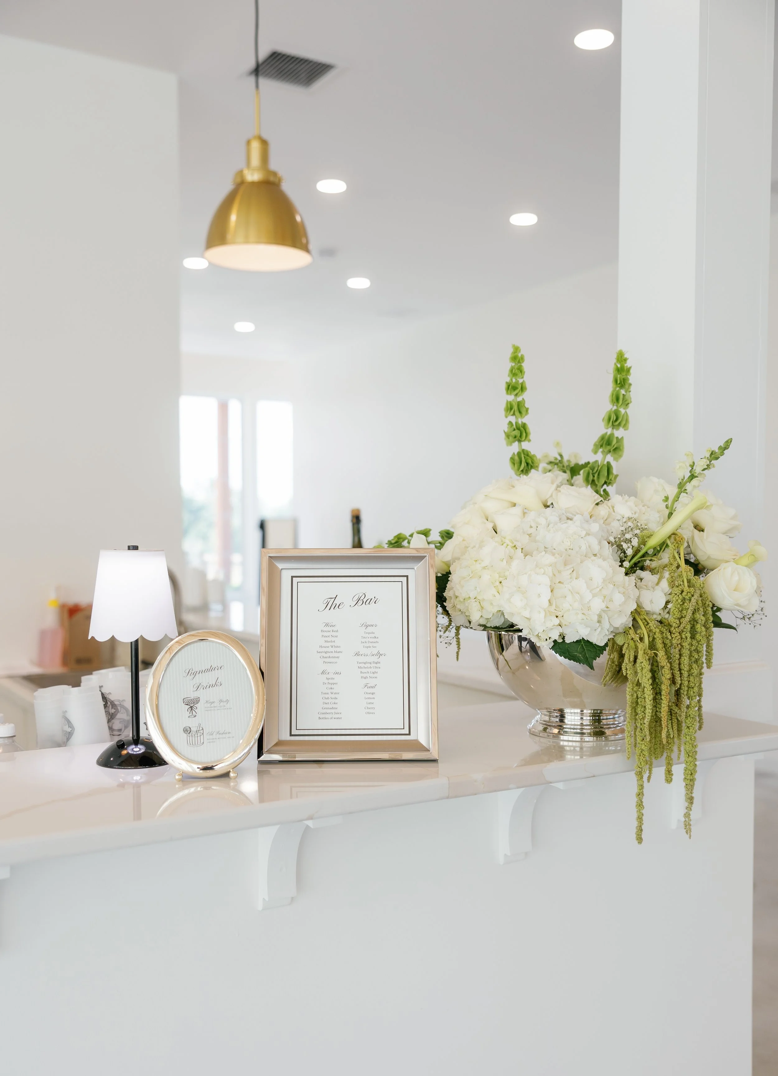 Elegant white floral arrangement on a reception counter with framed menus and signage for a bar.