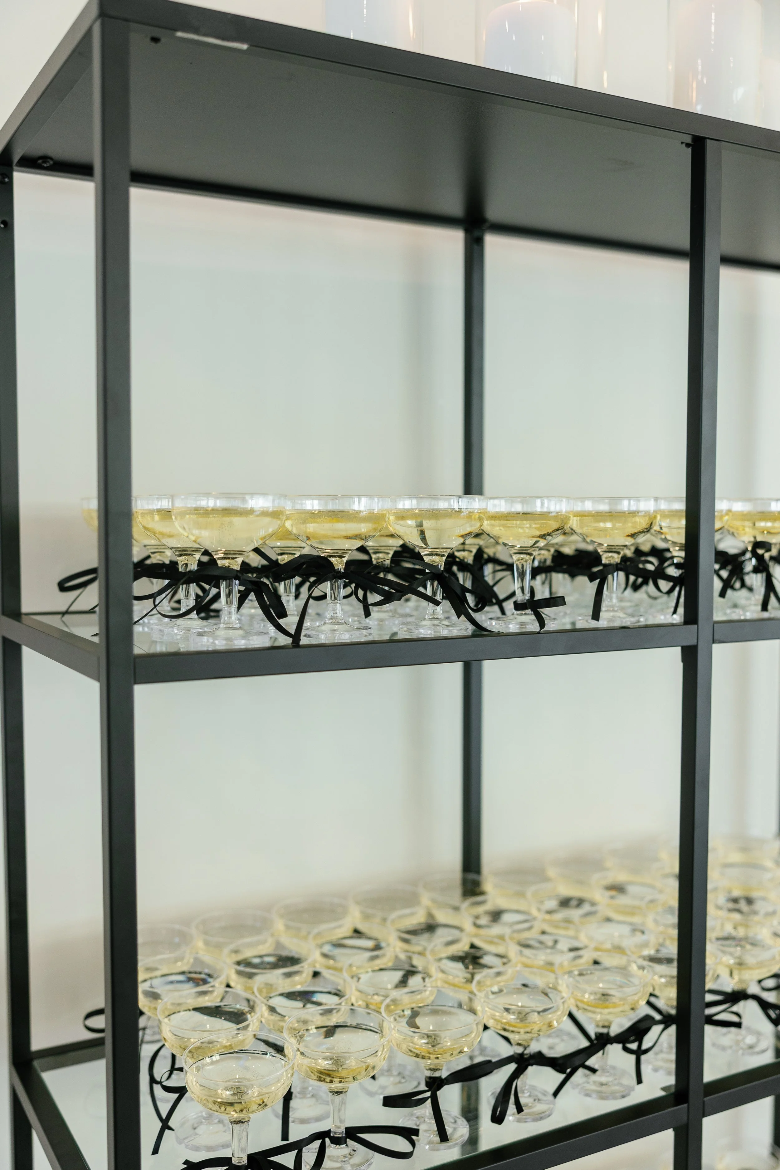 Several glasses of champagne with black ribbons tied around the stems, arranged on a black metal shelf.