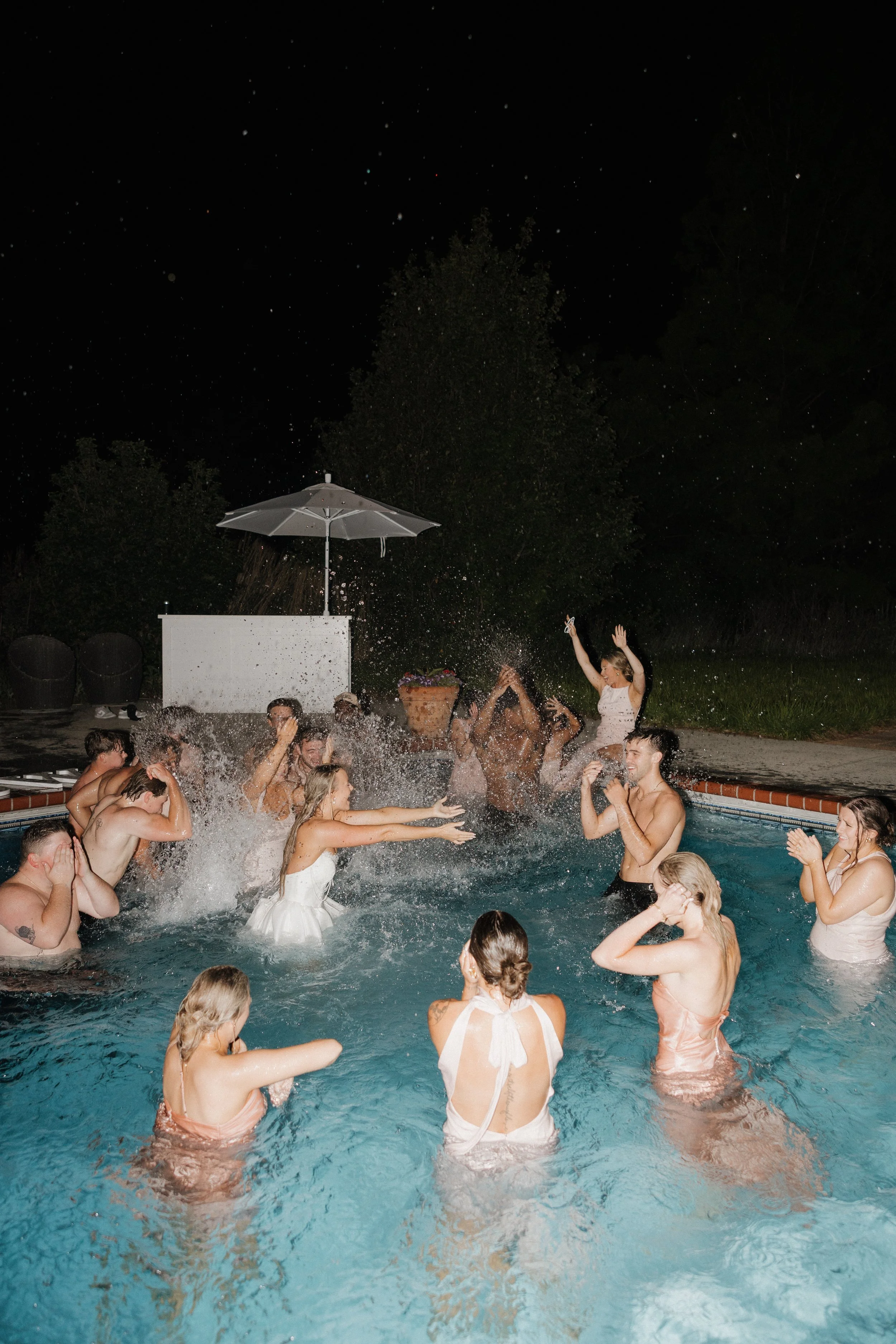 People celebrating in a swimming pool at night, splashing water, and dancing.