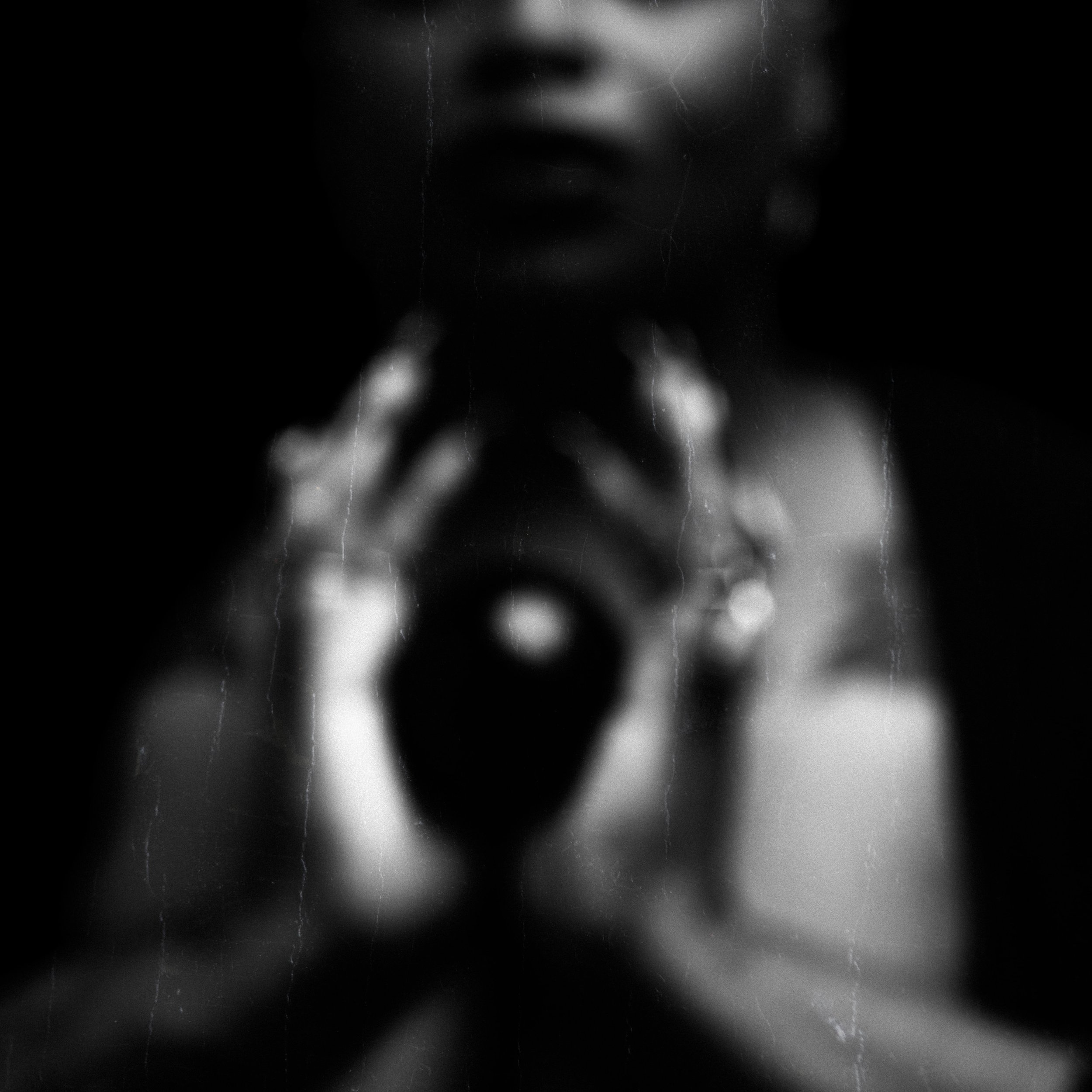 Blurred black and white photograph of a person taking a selfie in a mirror, with their face partially visible and holding a ring-shaped object.