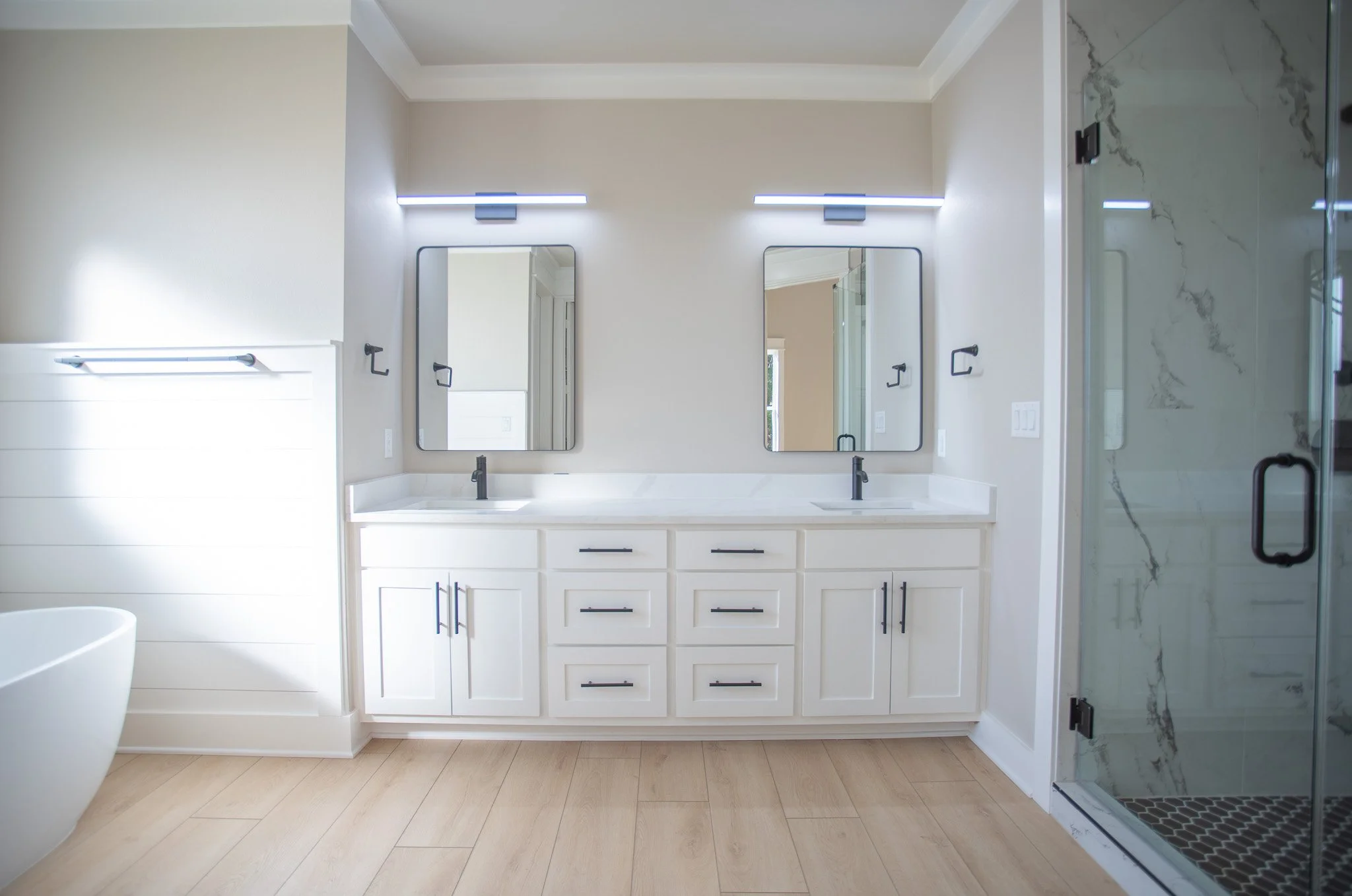 Modern bathroom with double vanity, two mirrors, black fixtures, and a glass-enclosed shower with marble tiles.