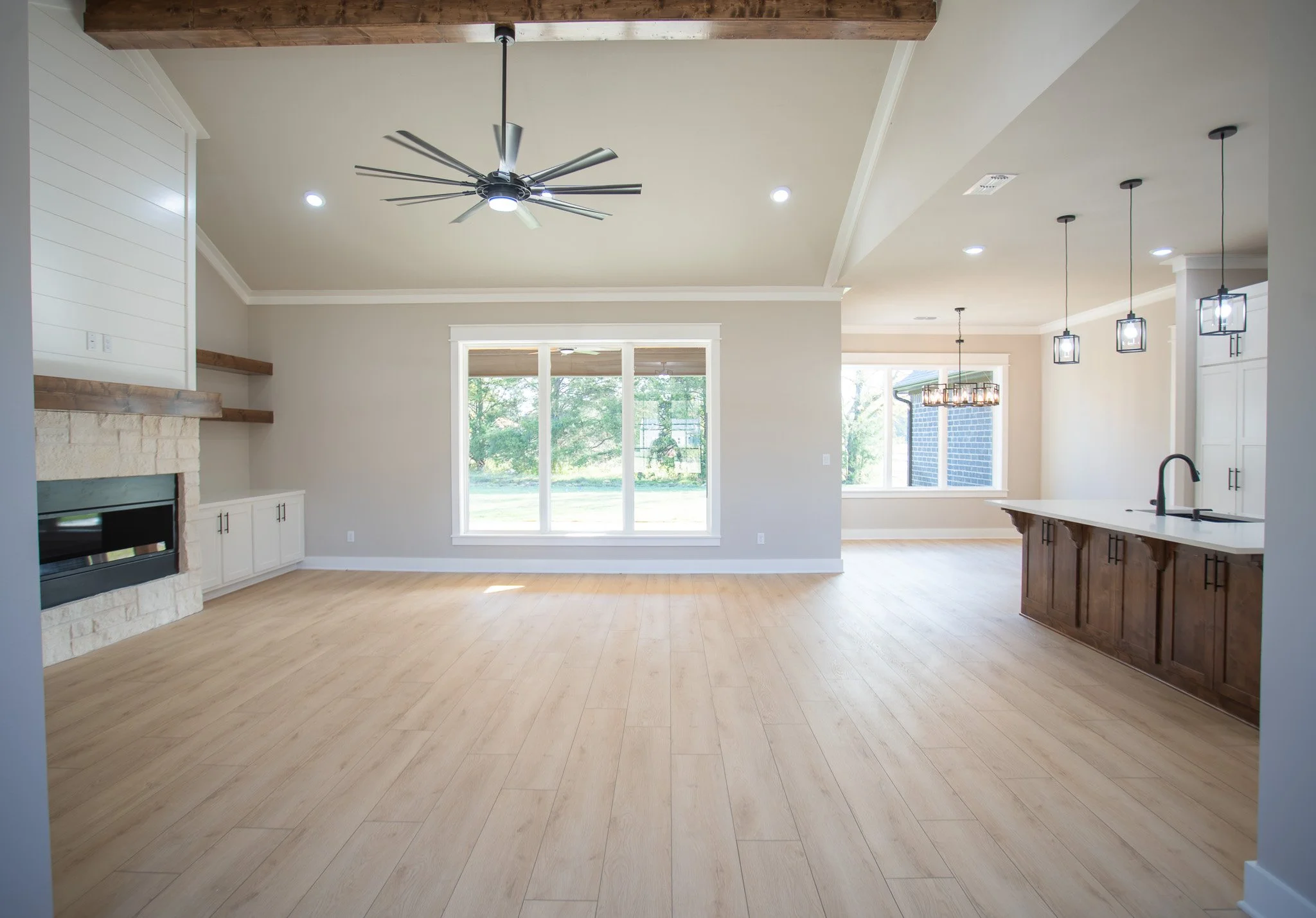 Open-concept living room and kitchen with large windows, wood floors, ceiling fan, and modern lighting fixtures.