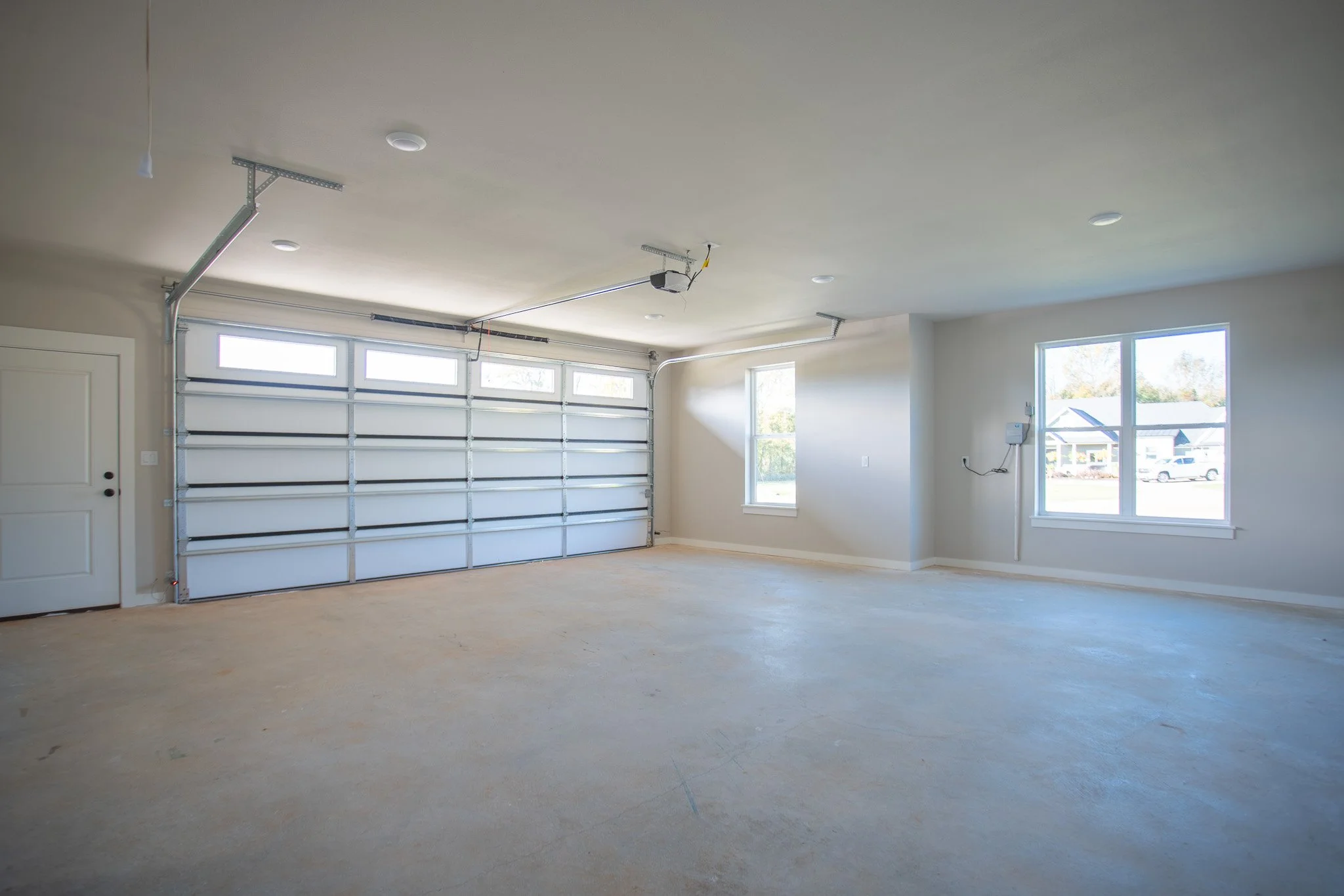 Empty residential garage with open white door, concrete floor, and two windows showing outdoors.