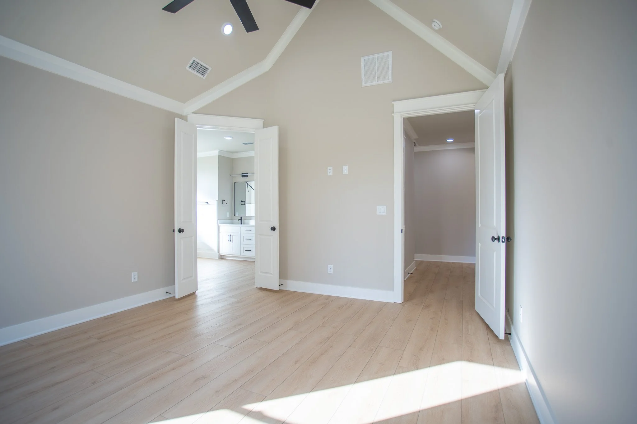 Empty living room with beige walls, wooden floor, white trim, and two open doors leading to different rooms.