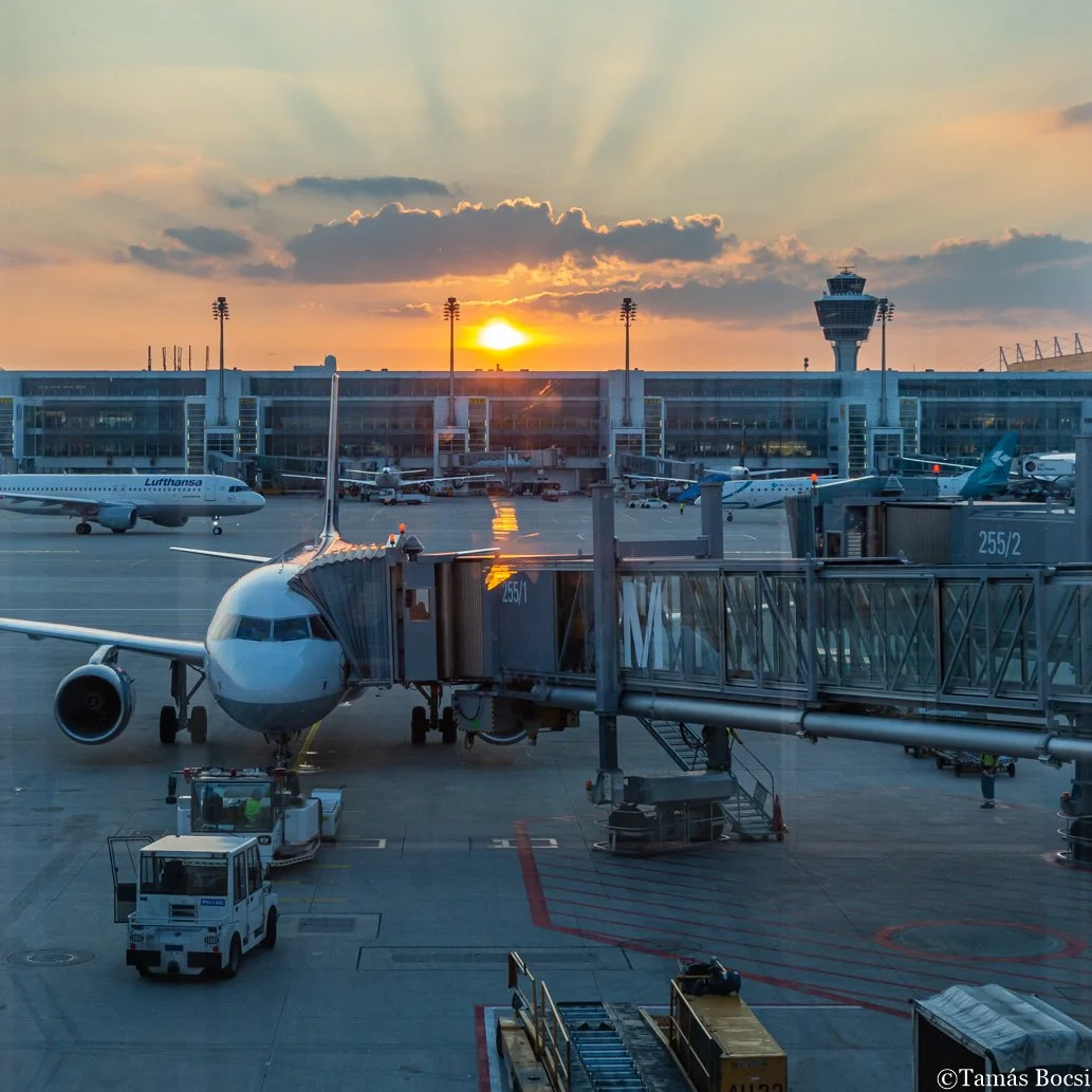An airplane at an airport gate during sunset, with other planes on the tarmac and the control tower in the background.
