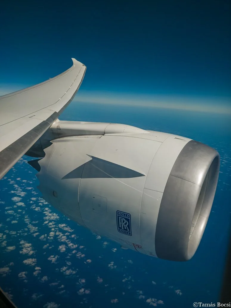 Photo taken from an airplane window showing the airplane's wing and engine, with clouds and the sky in the background.