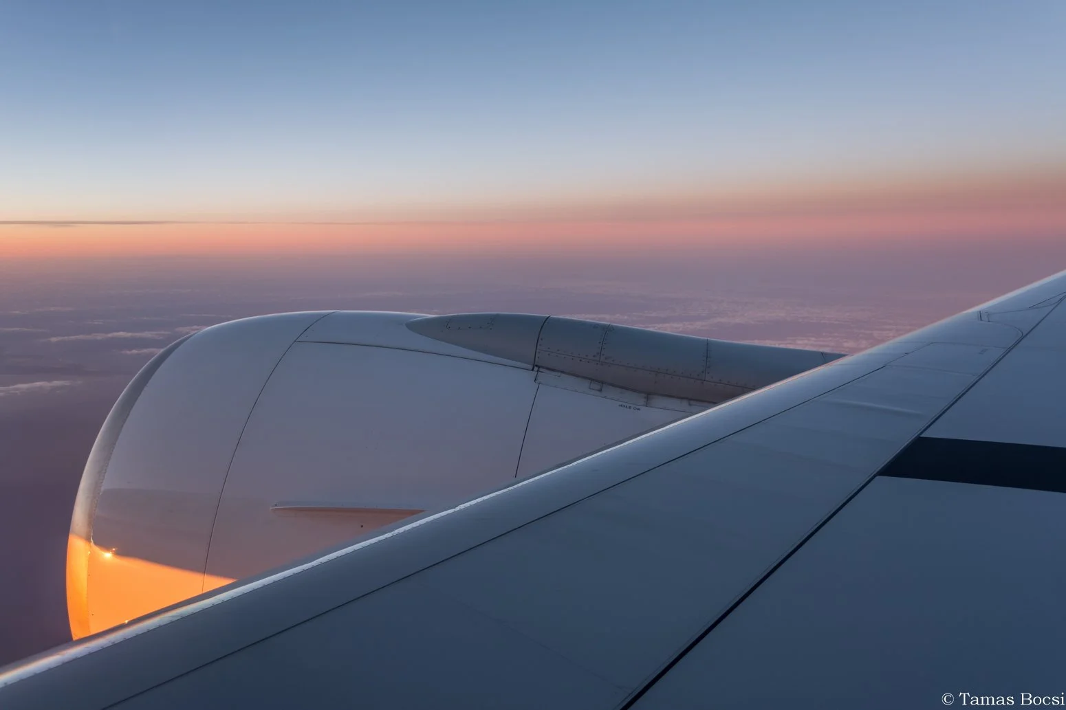 View of airplane wing and engine at sunset sky with colorful horizon